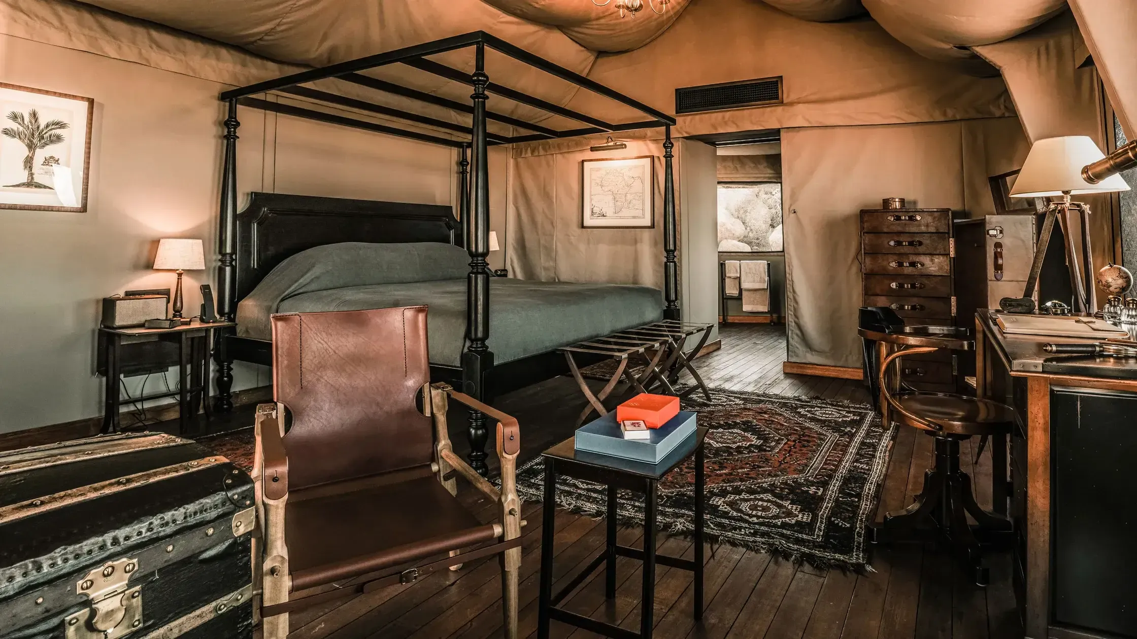 Zannier Sonop, Africa — Luxury safari tent bedroom with black four-poster bed, leather seating, warm ambient lighting, and vintage safari furnishings.