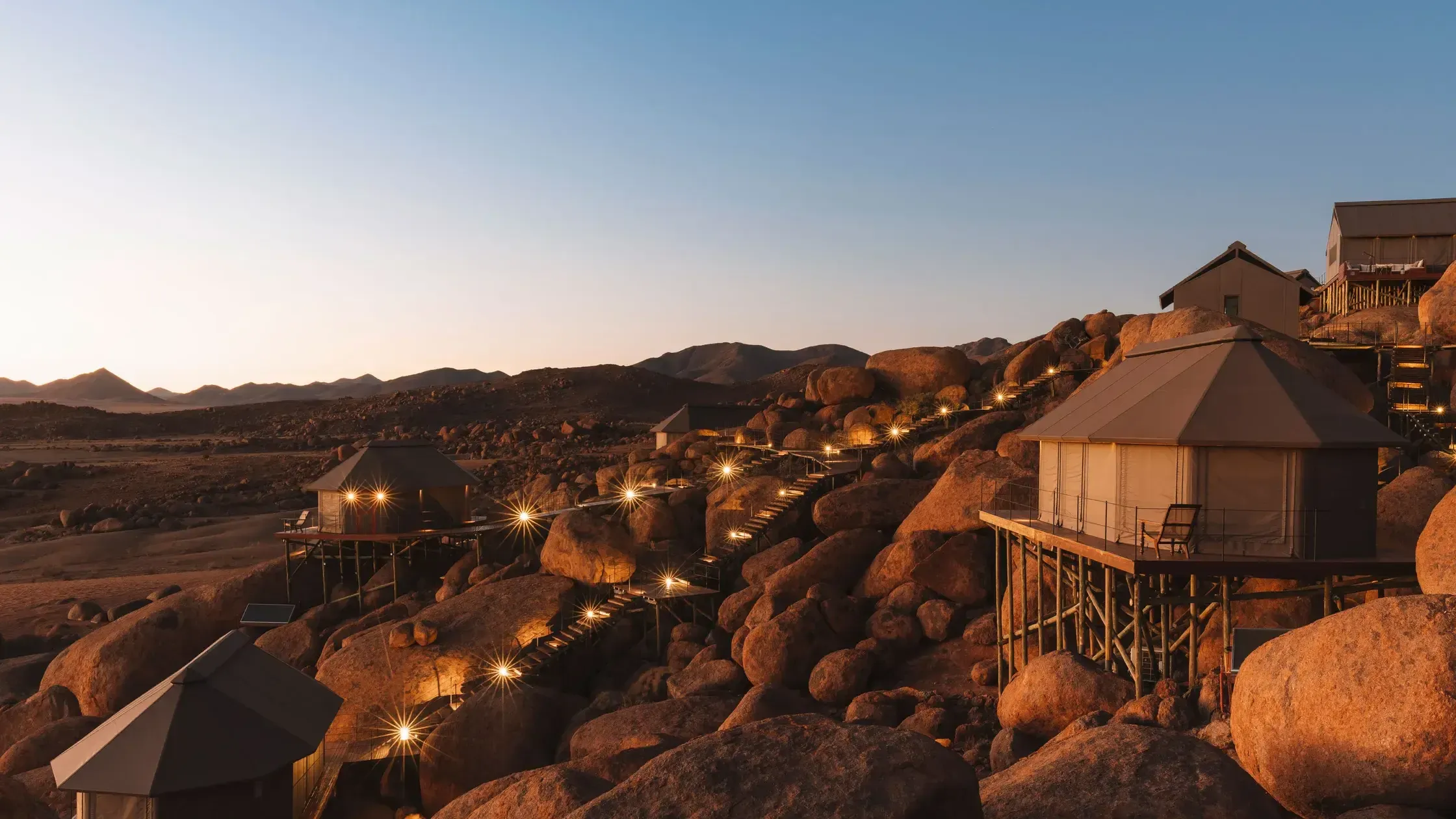 Zannier Sonop, Africa — Illuminated stone pavilions nestled among granite boulders at dusk, with stepped pathways and mountain vista.