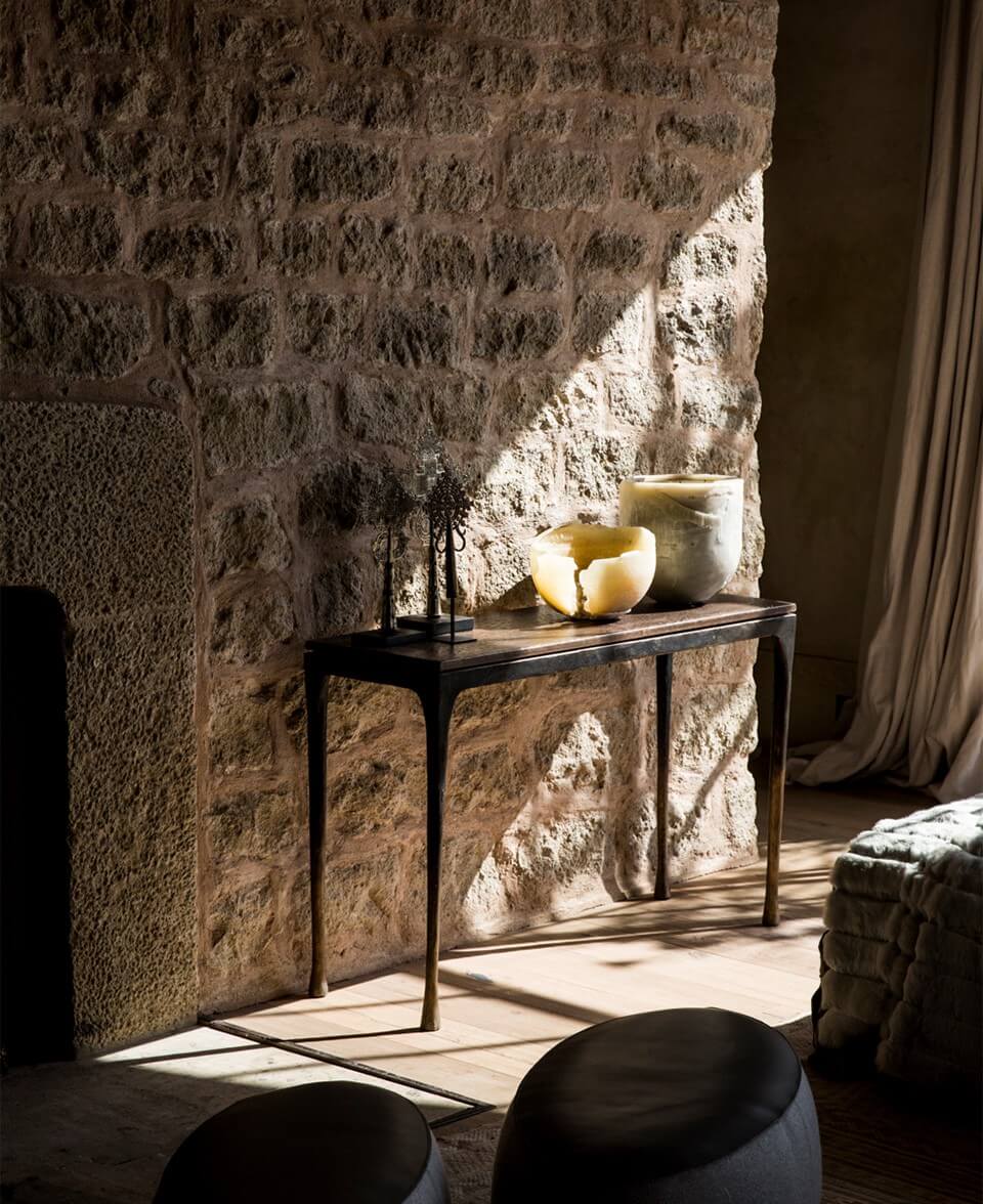 Arijiju Retreat, Africa — Stone villa interior with black console table, ceramic vessels, and natural light casting shadows on textured walls.