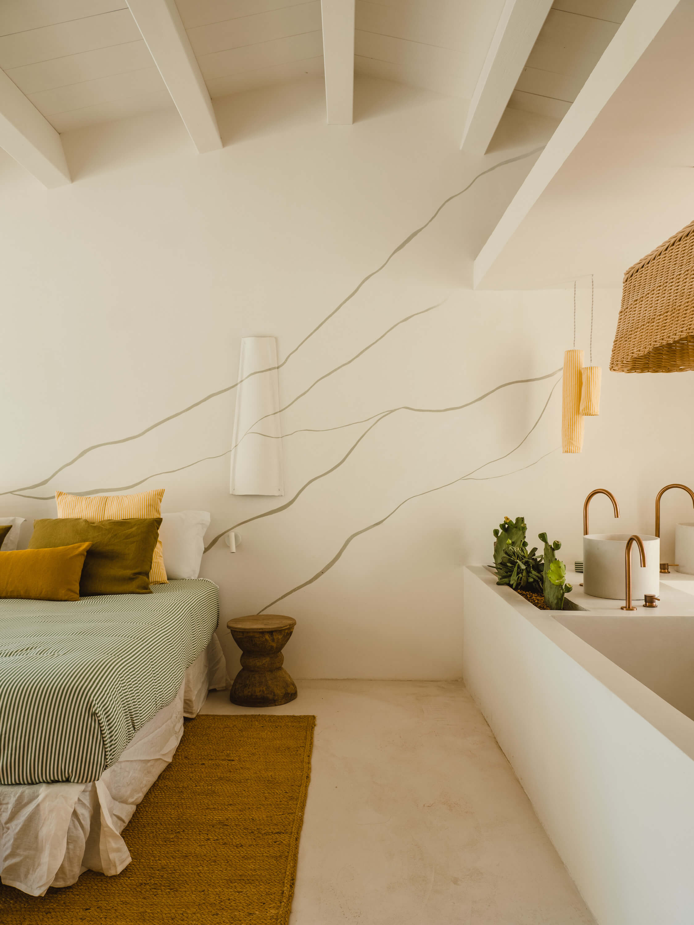 Morvedra Nou, Balearic Islands — Minimalist bedroom with wavy wall relief, warm textiles, brass fixtures, and ensuite bathroom in cream and natural materials.