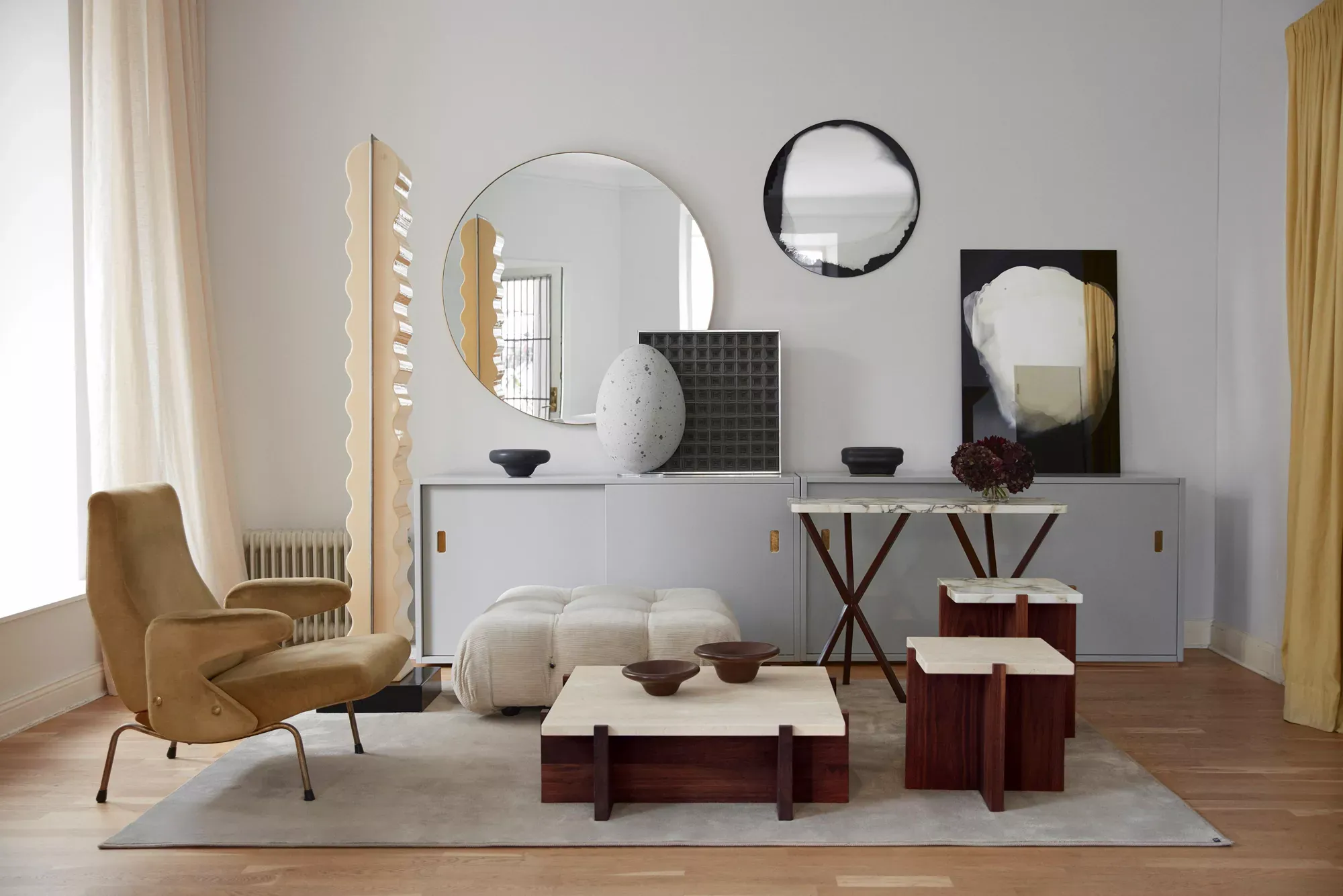 No Early Birds — Modern hospitality lounge with curved cream armchair, sculptural poufs, dark wood tables, mirrored wall displays, and warm natural light—No Early Birds, Europe.
