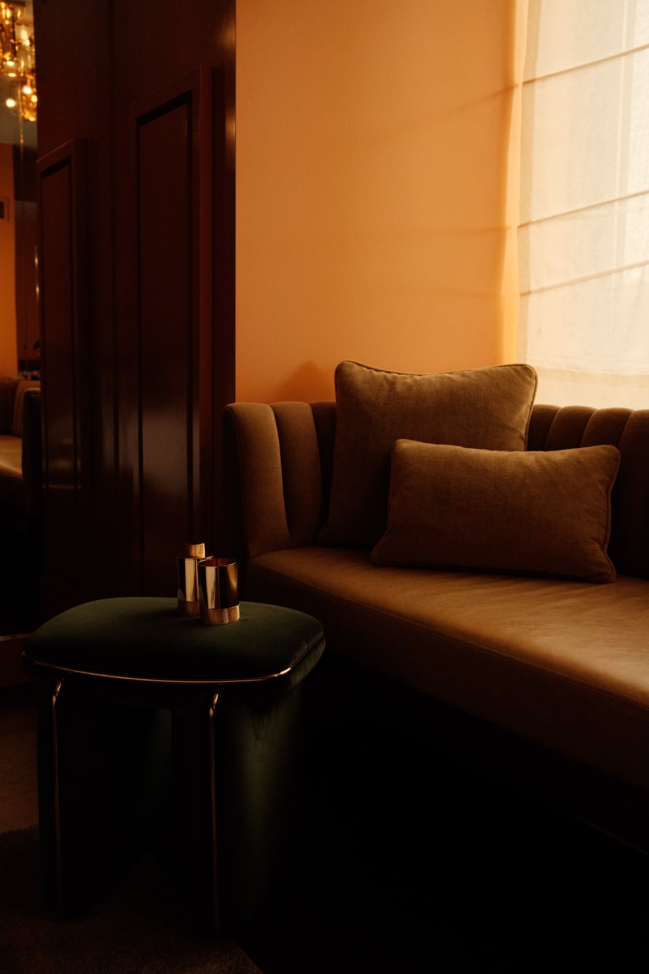 The Manner, North America — Warm-lit lounge with bronze armchair, black side table, ochre walls, and frosted glass window creating intimate luxury hospitality interior.