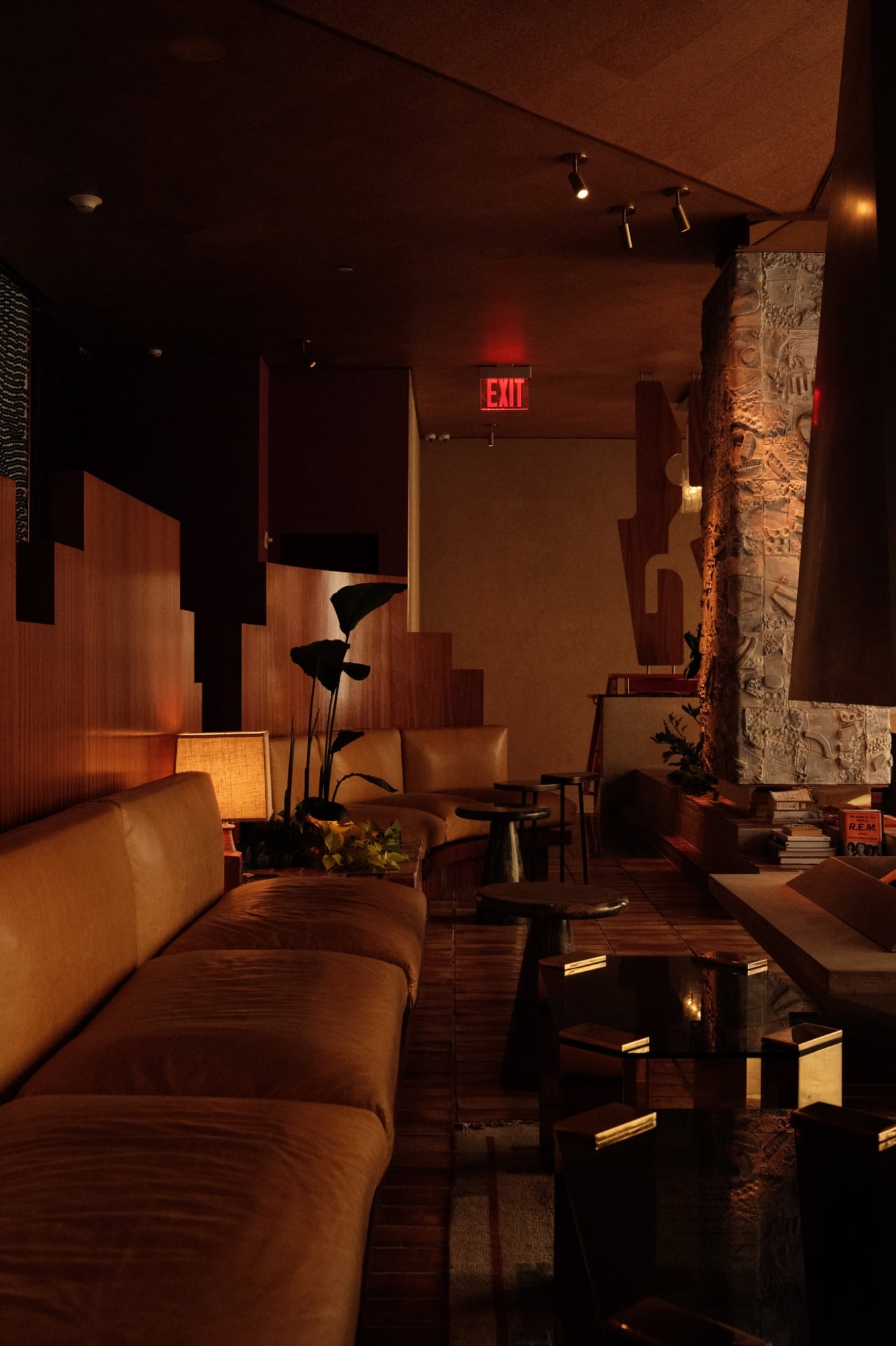 The Manner, North America — Warm-lit lounge with terracotta seating, sculptural floor lamps, textured stone column, and modernist architectural elements in ambient hospitality design.