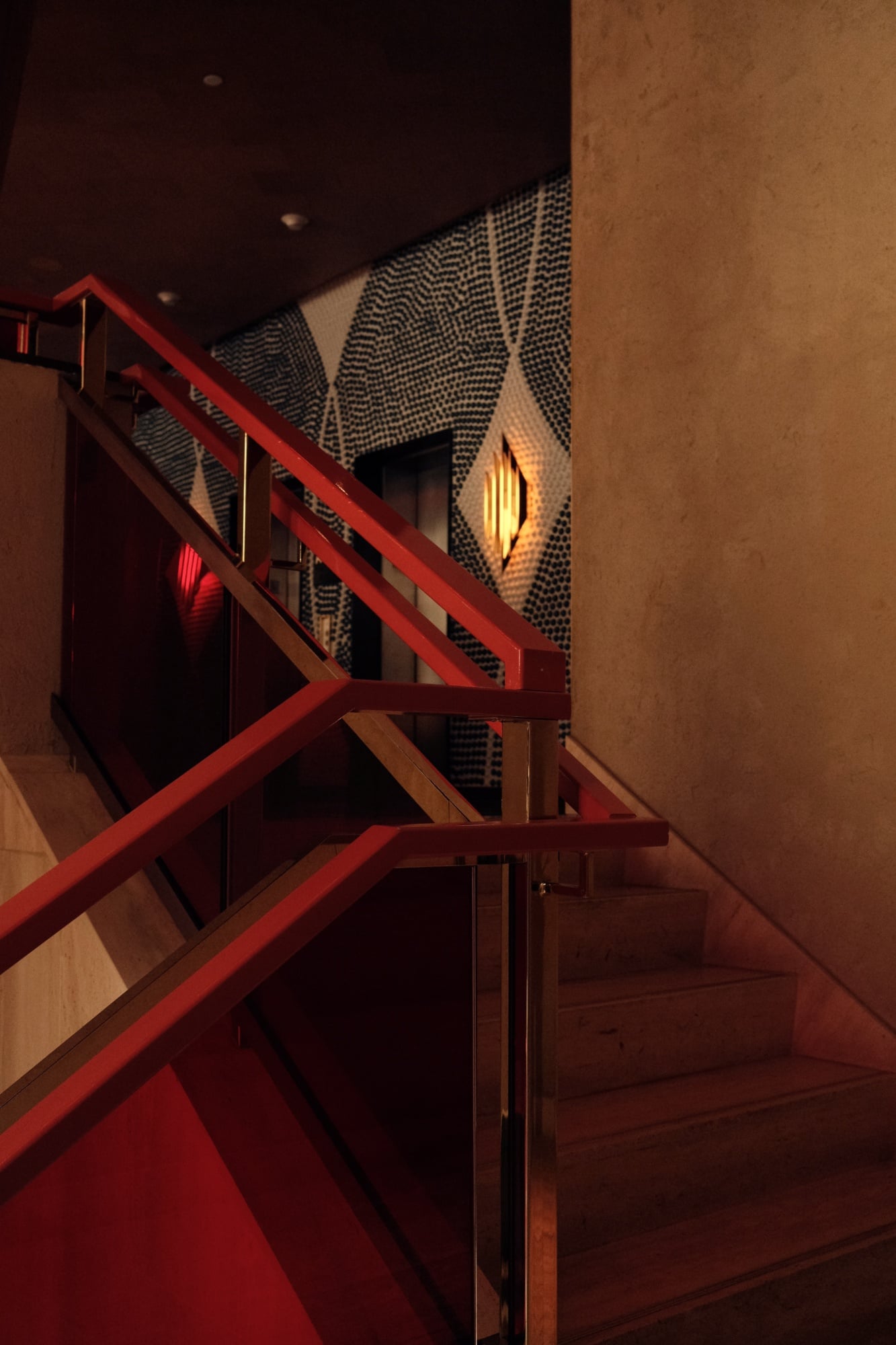 The Manner, North America — Red steel staircase with geometric perforated metal panel and warm accent lighting against terracotta wall at night.