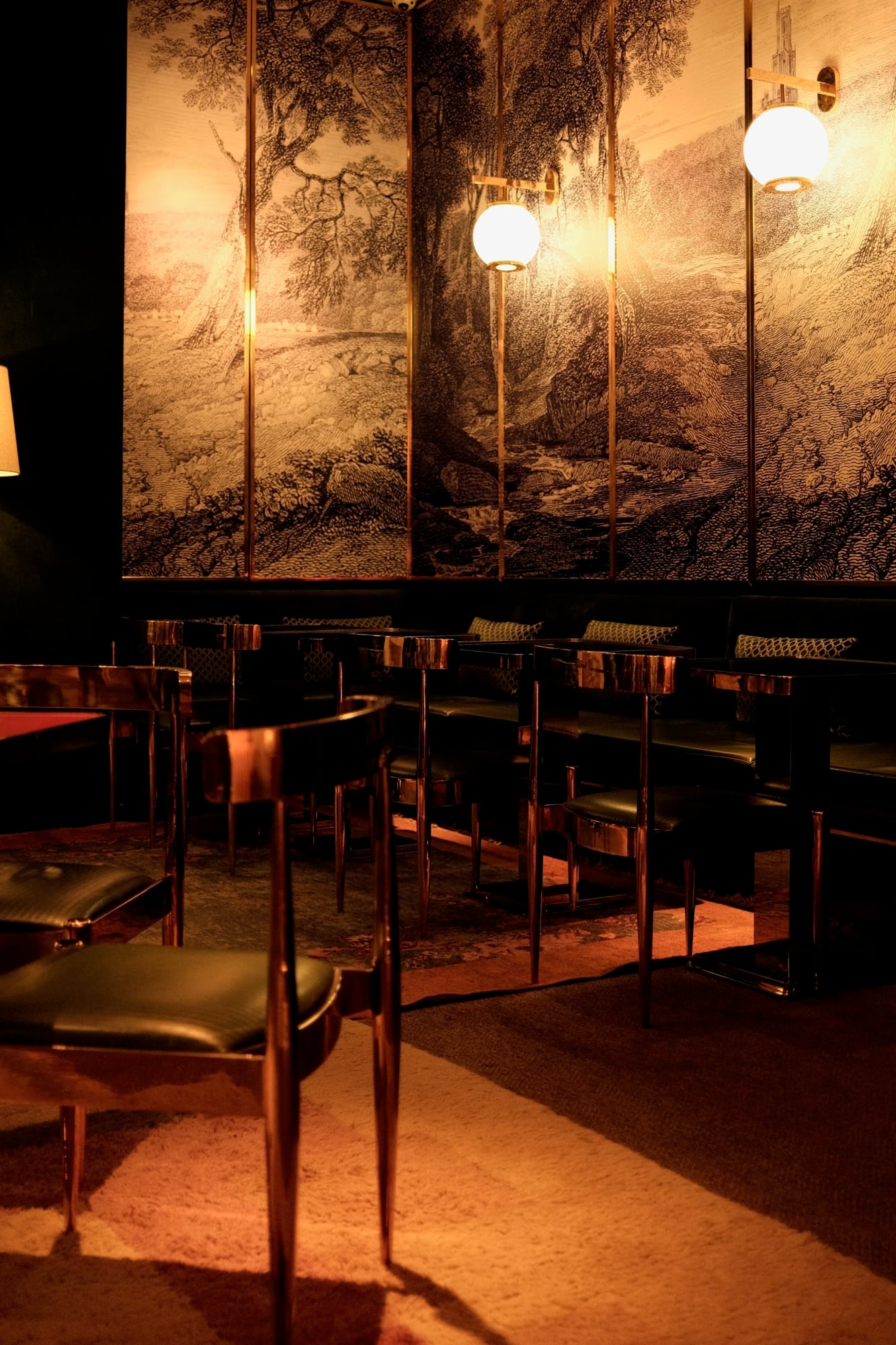 The Manner, North America — Mid-century modern dining chairs beneath forest mural panels, warm ambient lighting, minimalist luxury hospitality interior.