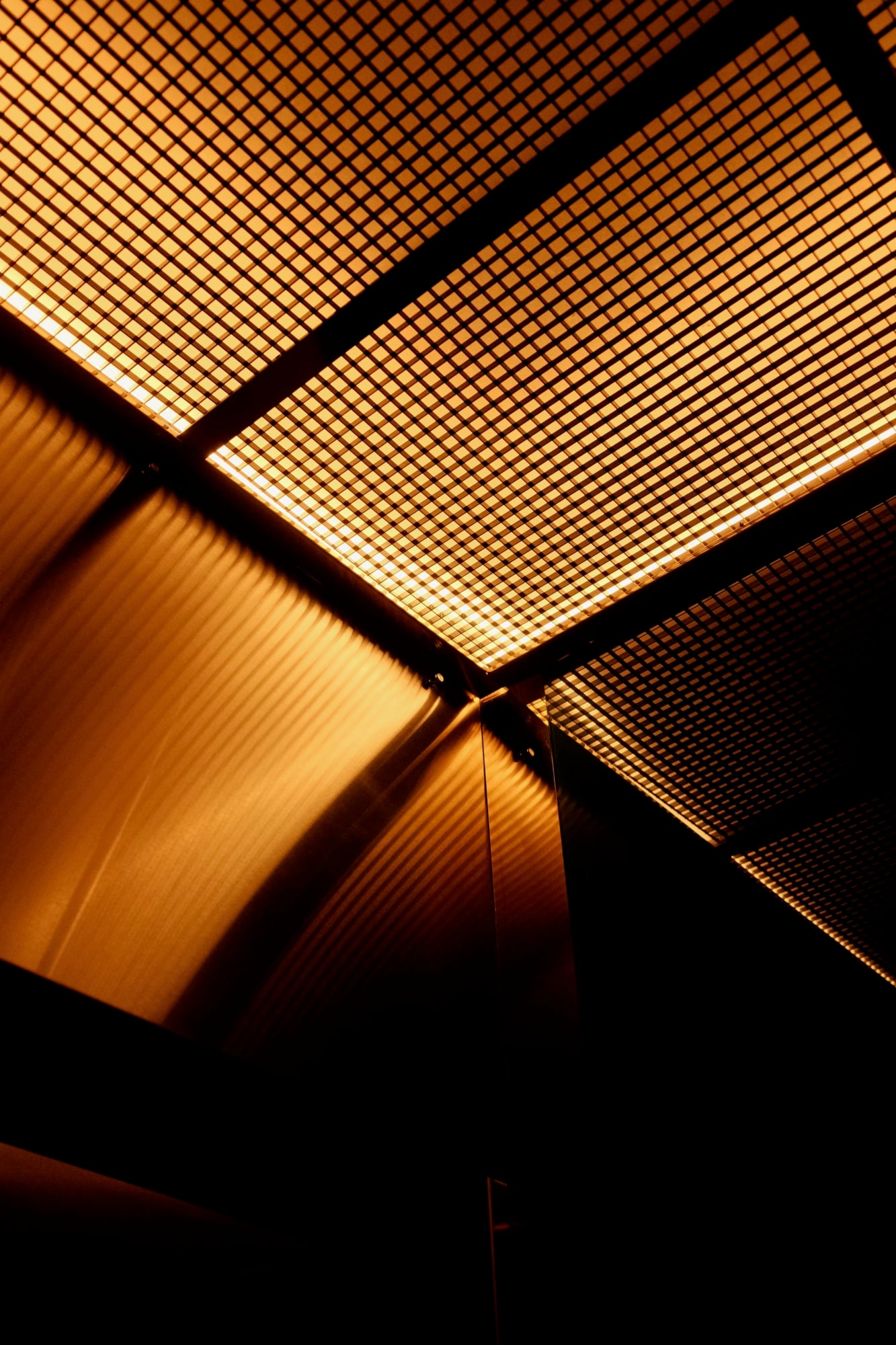 The Manner, North America — Geometric ceiling panels with warm amber LED backlighting and architectural gridwork creating layered ambient light in modern luxury interior design.