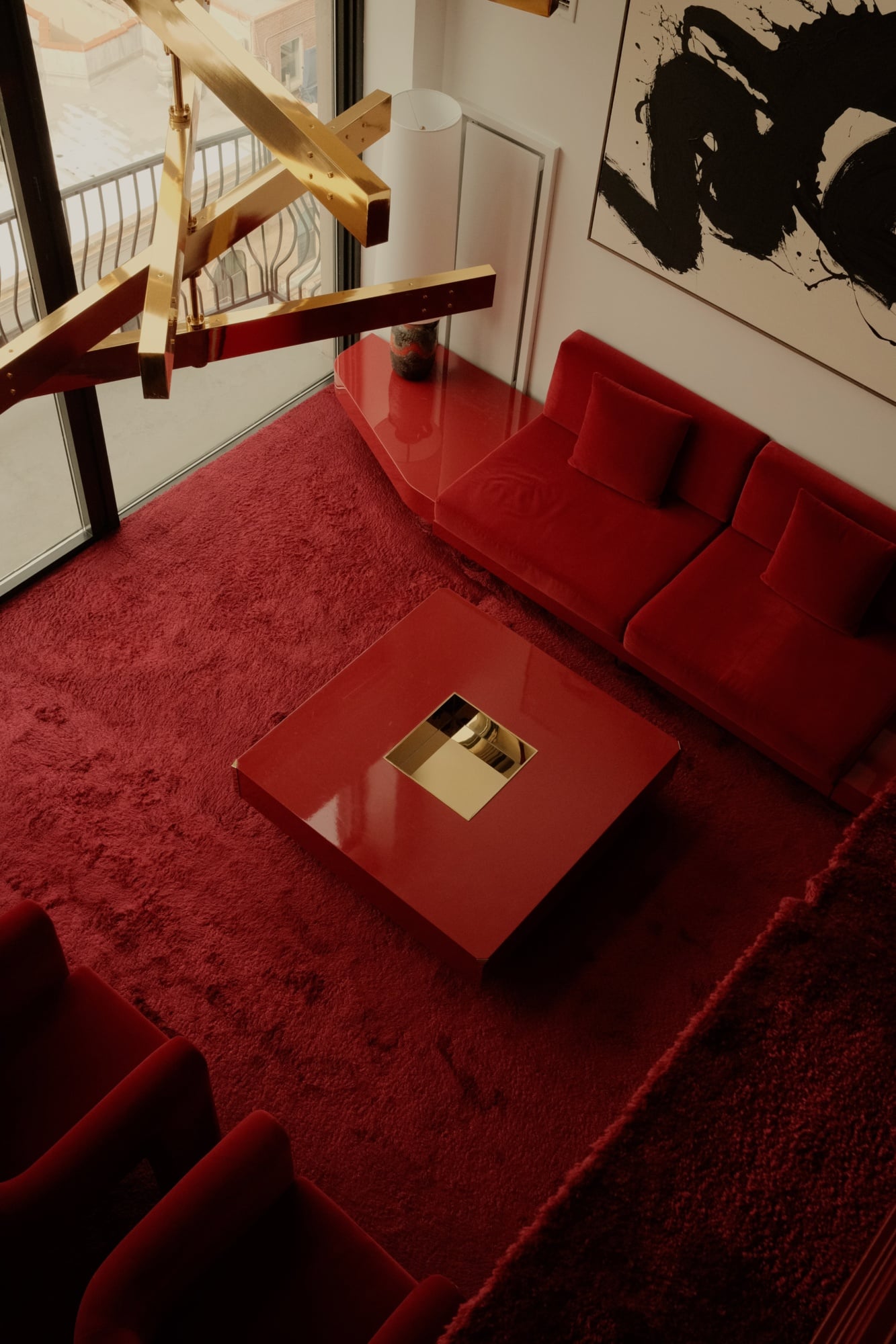 The Manner, North America — Red velvet seating and carpet with geometric wood sculptural installation, minimalist black and white artwork, and glass coffee table in contemporary luxury hotel lounge.