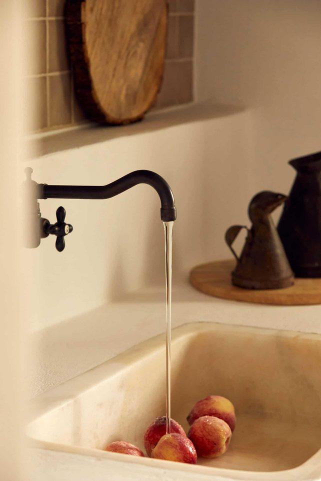 The Rooster, Europe — Minimalist bathroom sink with black vintage faucet, terracotta vessels, and fresh peaches in warm natural light.