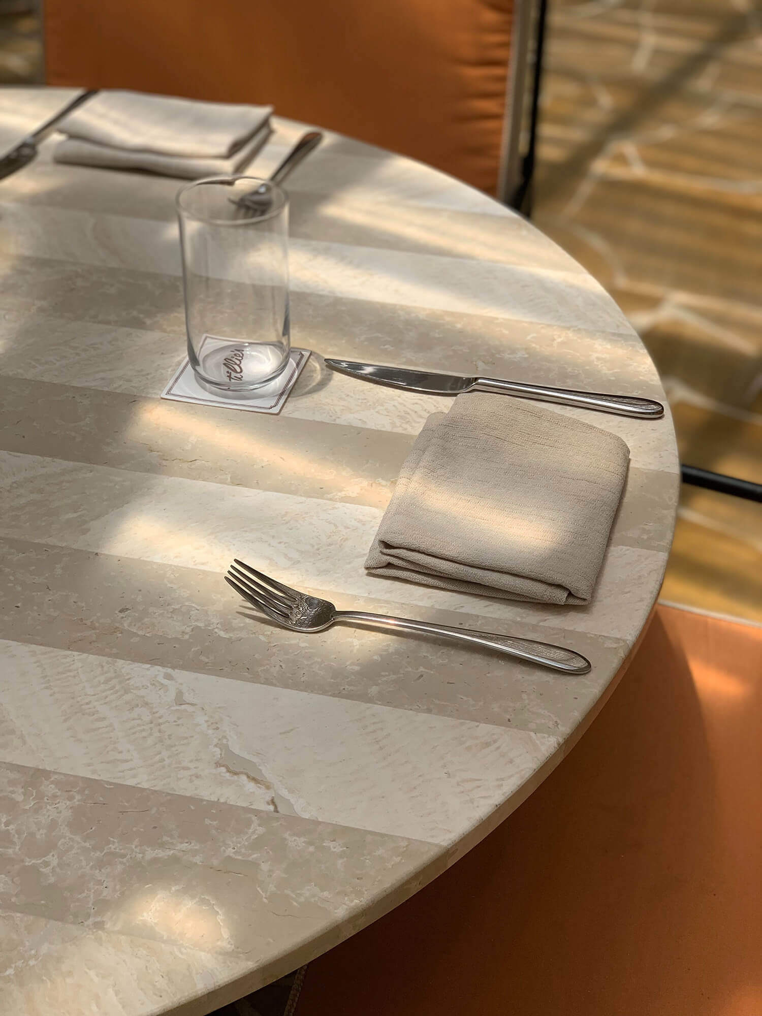 Palm Heights, North America — Minimalist marble dining table set with folded linen napkin, polished flatware, and water glass in natural light.