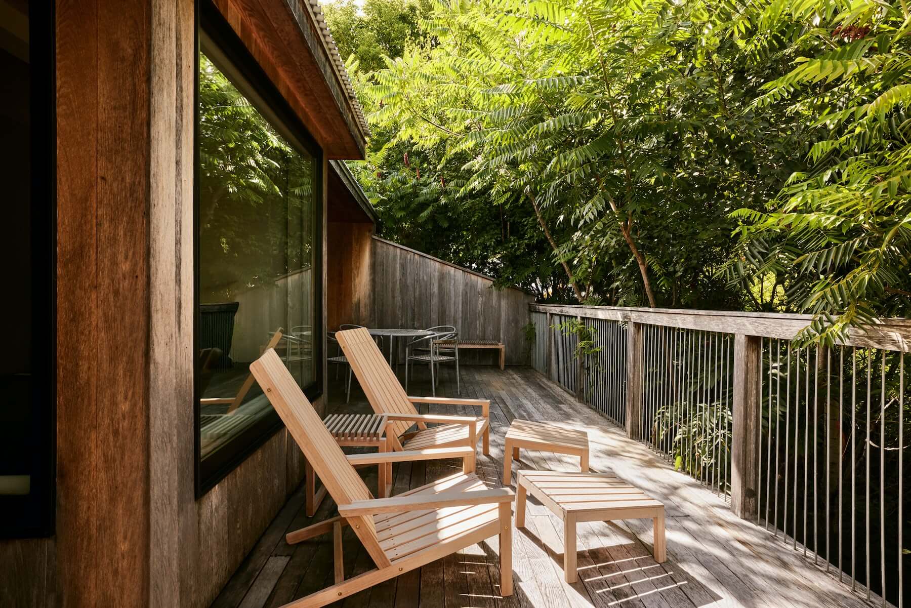 Tourists, North America — Wooden deck with lounge chairs overlooking lush forest, featuring modern architecture and natural light through floor-to-ceiling windows.