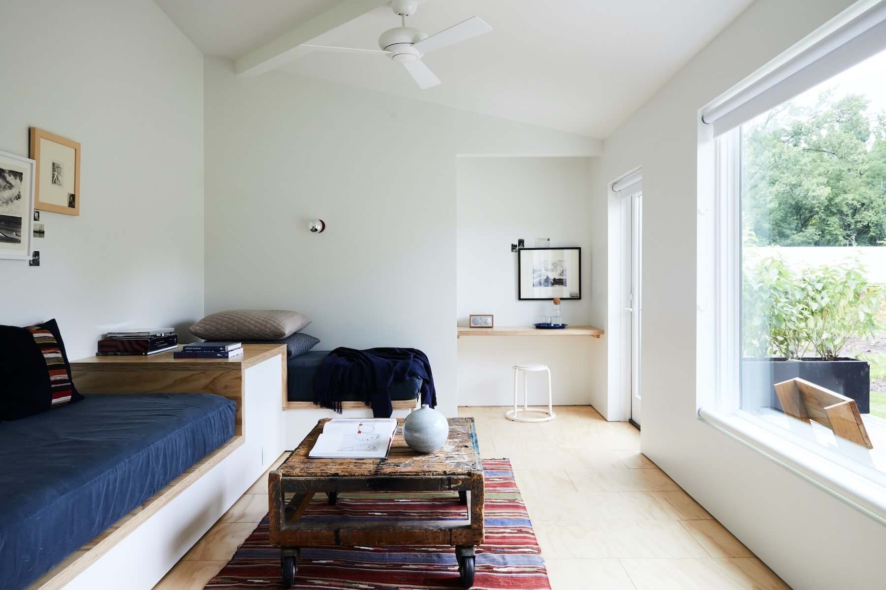 Tourists, North America — Minimalist bedroom with twin beds, wooden platform frames, white walls, large windows, natural light, contemporary furnishings, and curated artwork.