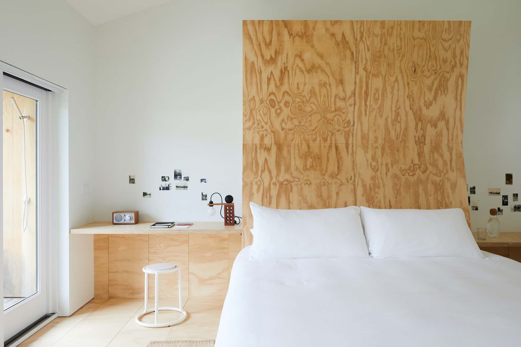 Tourists Hotel North America — Minimalist bedroom with plywood accent wall, light oak desk, white bedding, and natural wood flooring creating serene Scandinavian-inspired aesthetic.