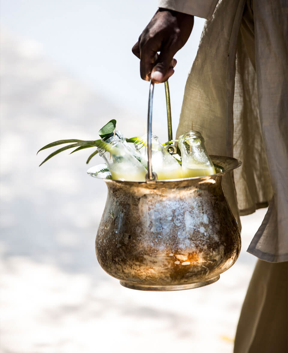 Arijiju Retreat, Africa — Hand holding brass vessel with fresh catch and herbs against clouded sky, artisanal hospitality detail.