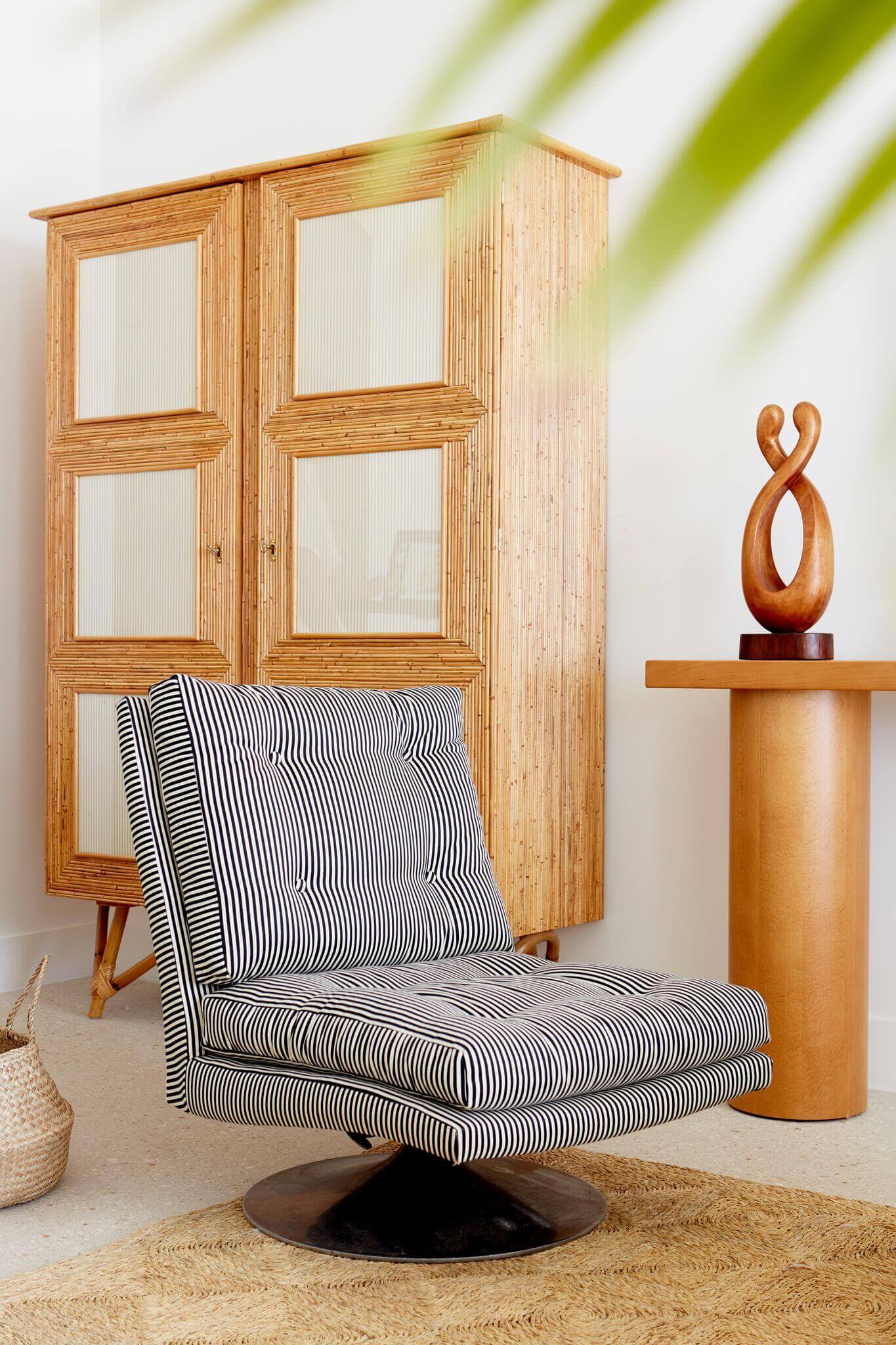 Palm Heights, North America — Mid-century modern lounge chair with black and white striped upholstery, wooden pedestal table, sculptural art object, and glazed timber wardrobe in minimalist interior with natural light.