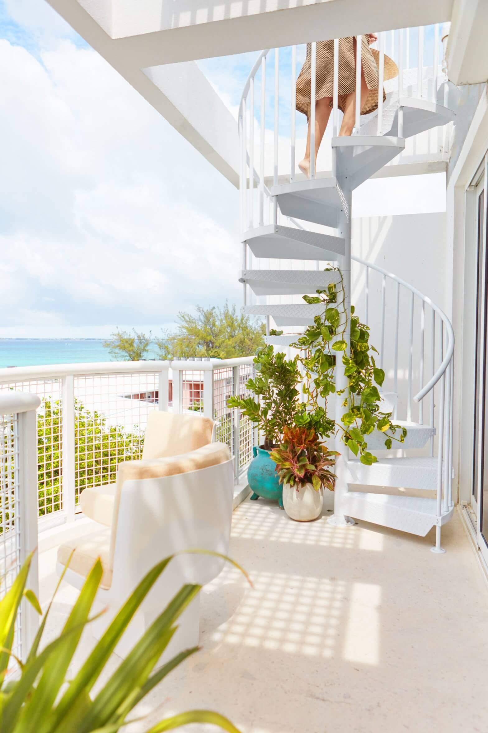 Palm Heights, North America — Spiral staircase with white railings, coastal ocean views, potted plants, and minimalist beach architecture in bright sunlight.