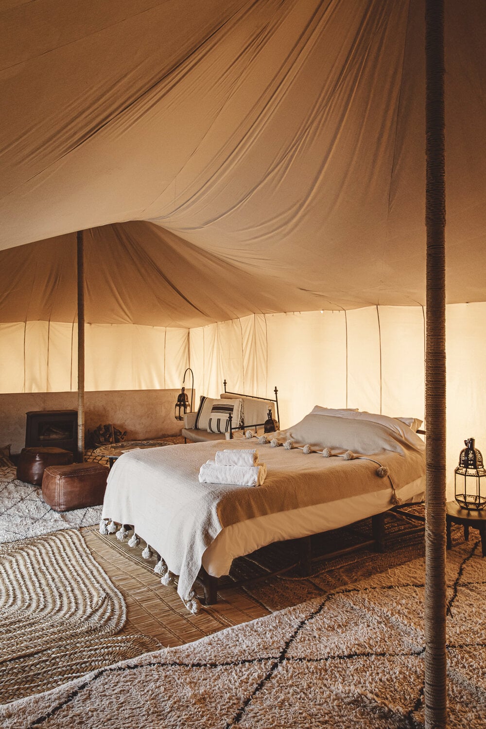 Scarabeo Camp, Africa — Candlelit luxury desert tent interior with twin beds, woven rugs, brass fixtures, and cream canvas draped ceiling.