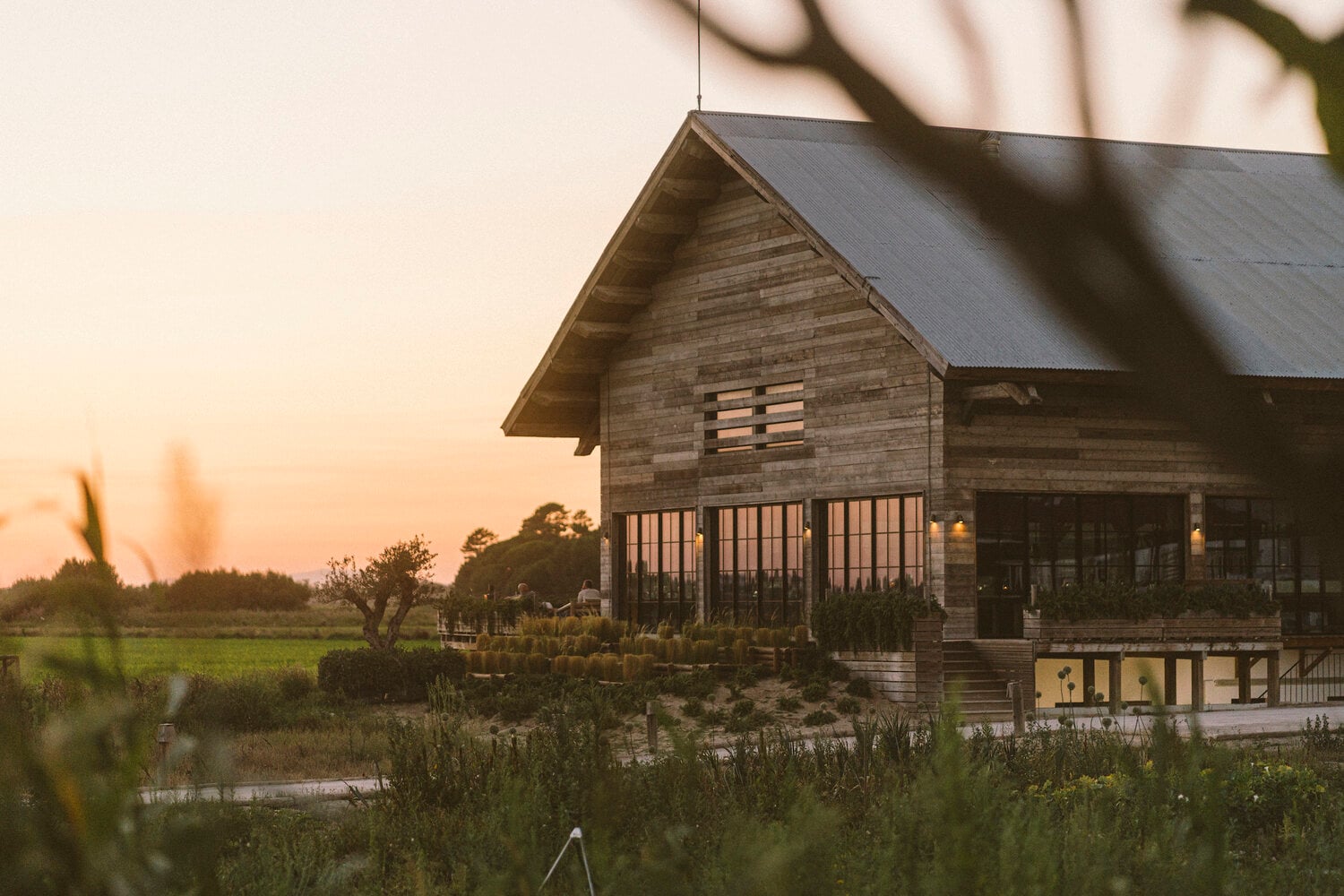 Quinta da Comporta, Europe — Elevated wooden lodge at dusk with metal railings, weathered timber siding, and expansive marshland views across still water.