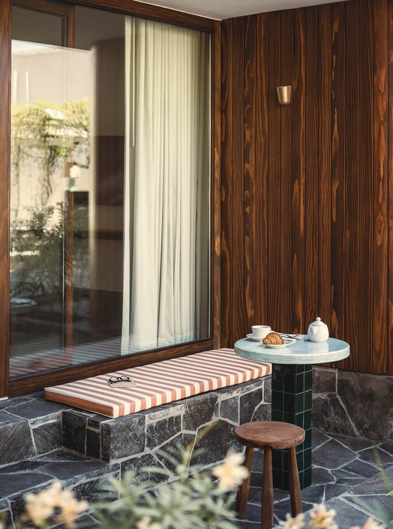 Baja Club, Mexico — Striped bench seating with stone base, marble side table, and dark wood-paneled wall overlooking garden courtyard.