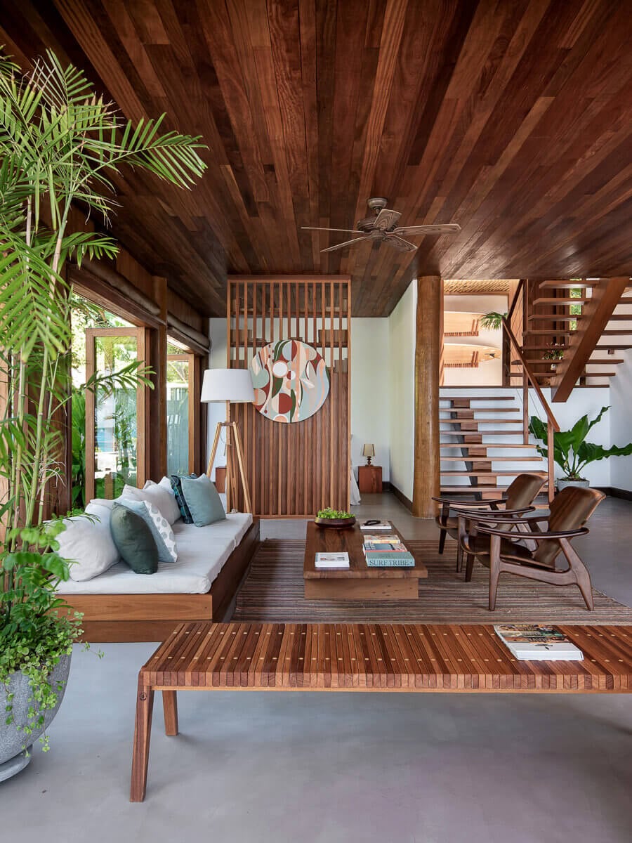 Barracuda Hotel & Villas, South America — Wood-lined living room with teak ceiling, lounge seating, sculptural staircase, potted palms, and open-air veranda overlooking tropical grounds.