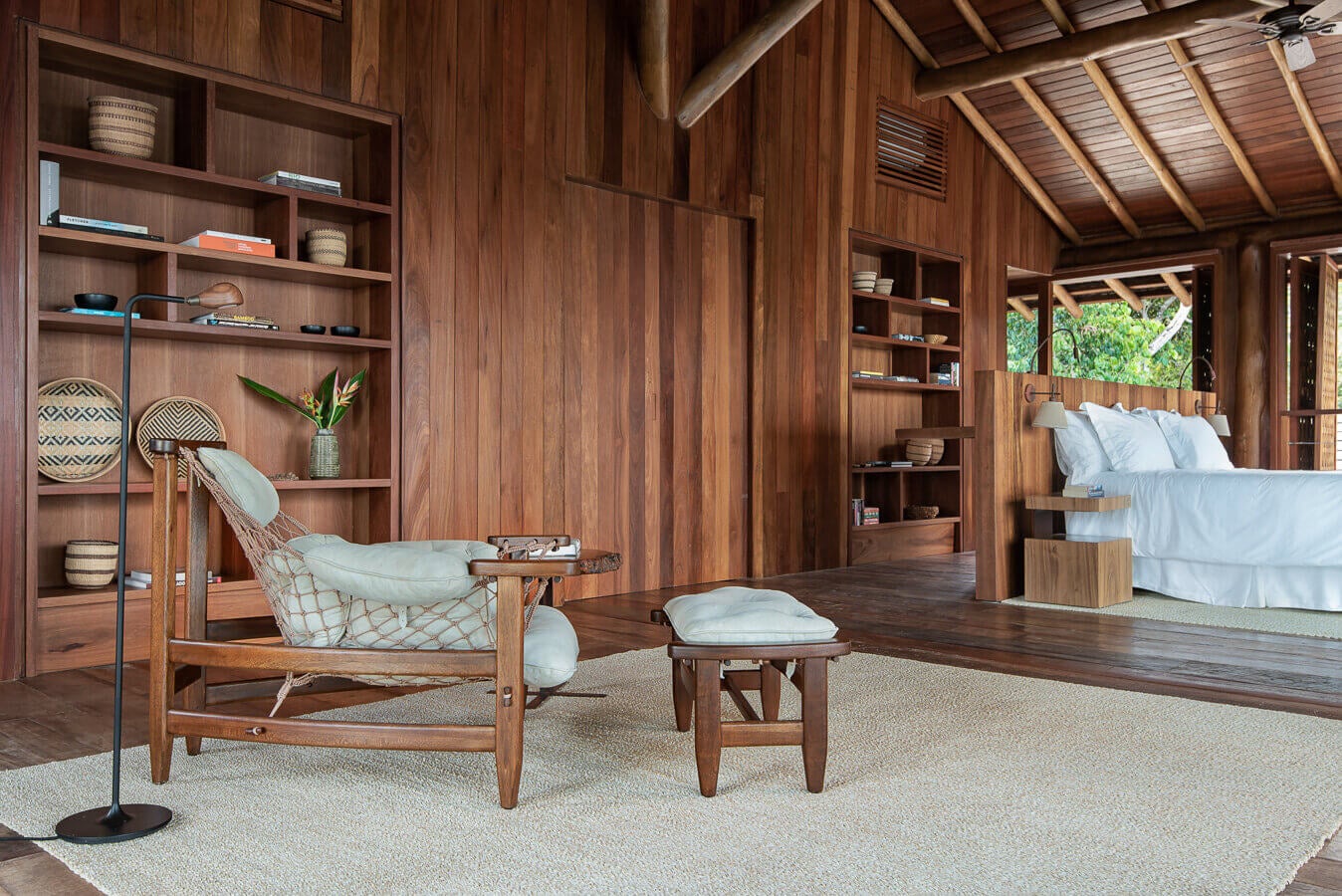 Barracuda Hotel & Villas, South America — Wooden pavilion bedroom with teak walls, built-in shelving, linen chair, and ocean views through open-air architecture.