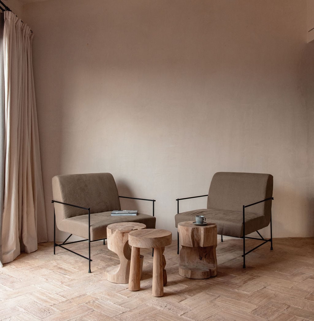 Son Vell, Balearic Islands — Minimalist seating area with taupe linen chairs, black metal frames, and natural wood stools in bright gallery space.