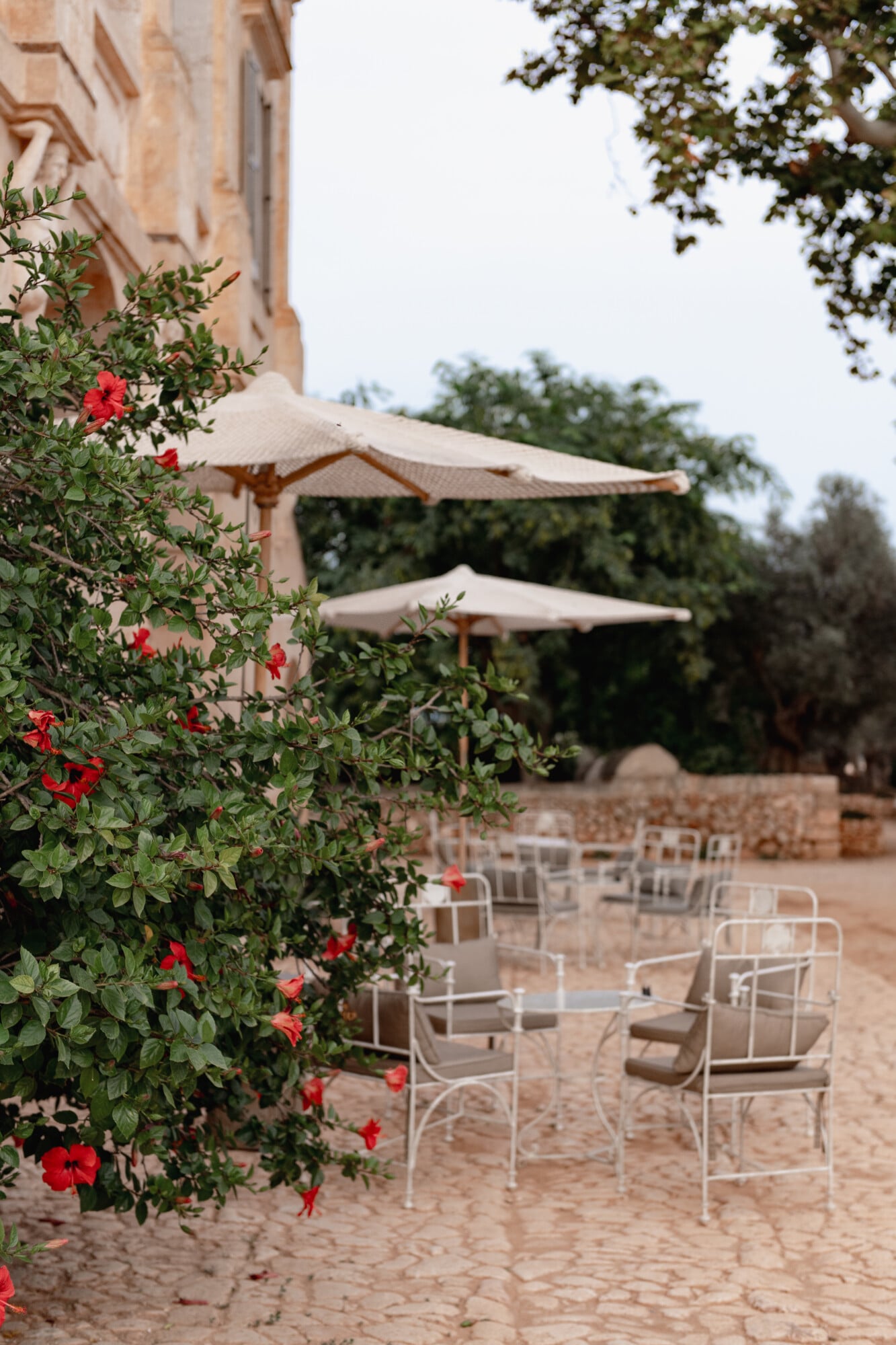 Son Vell, Balearic Islands — Terracotta courtyard with red flowering vines, white metal chairs, beige umbrellas, and stone architecture at dusk.