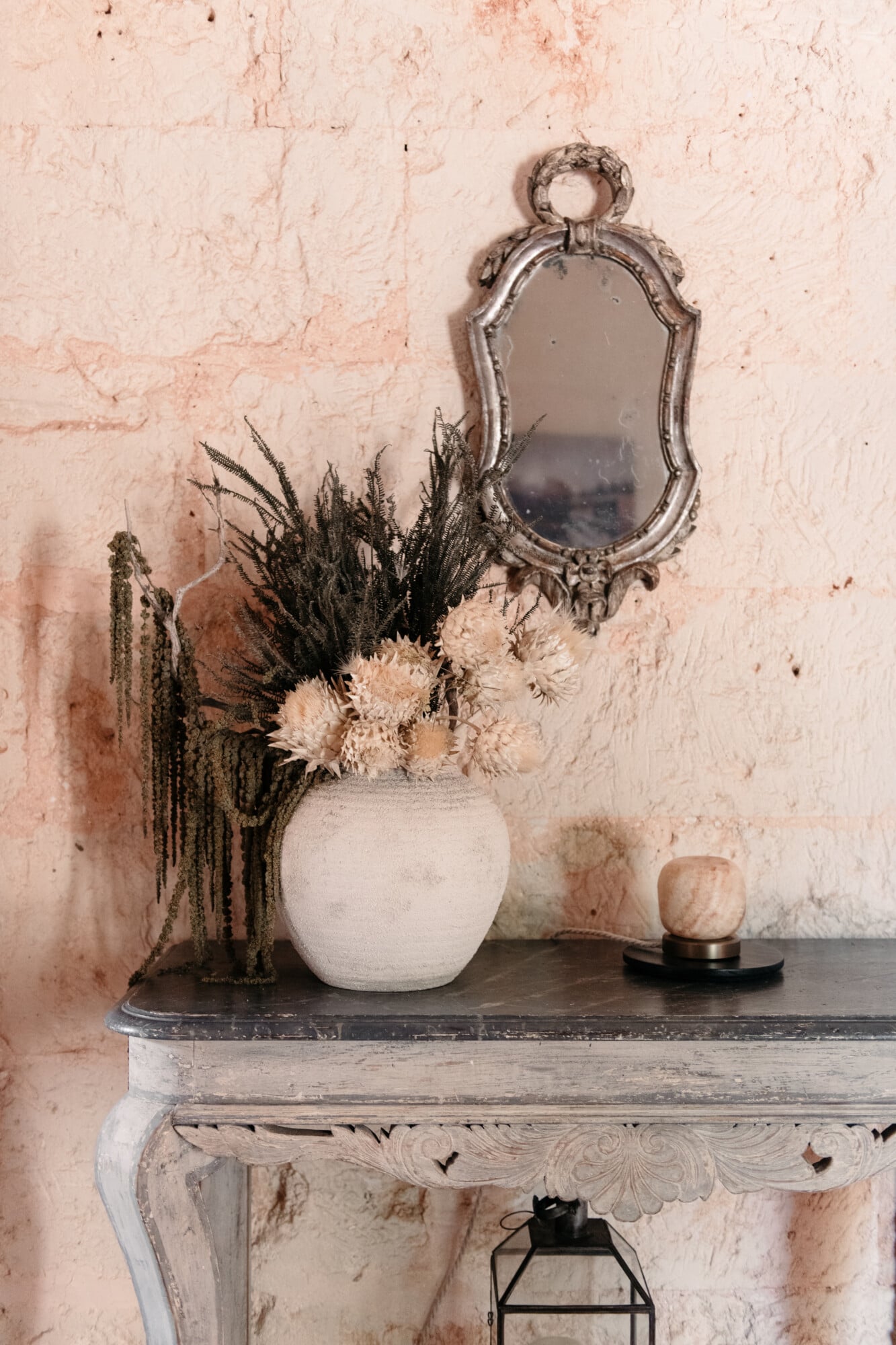 Son Vell, Balearic Islands — Ornate silver mirror above weathered console table with dried flower arrangement in ceramic vase, terracotta textured wall.