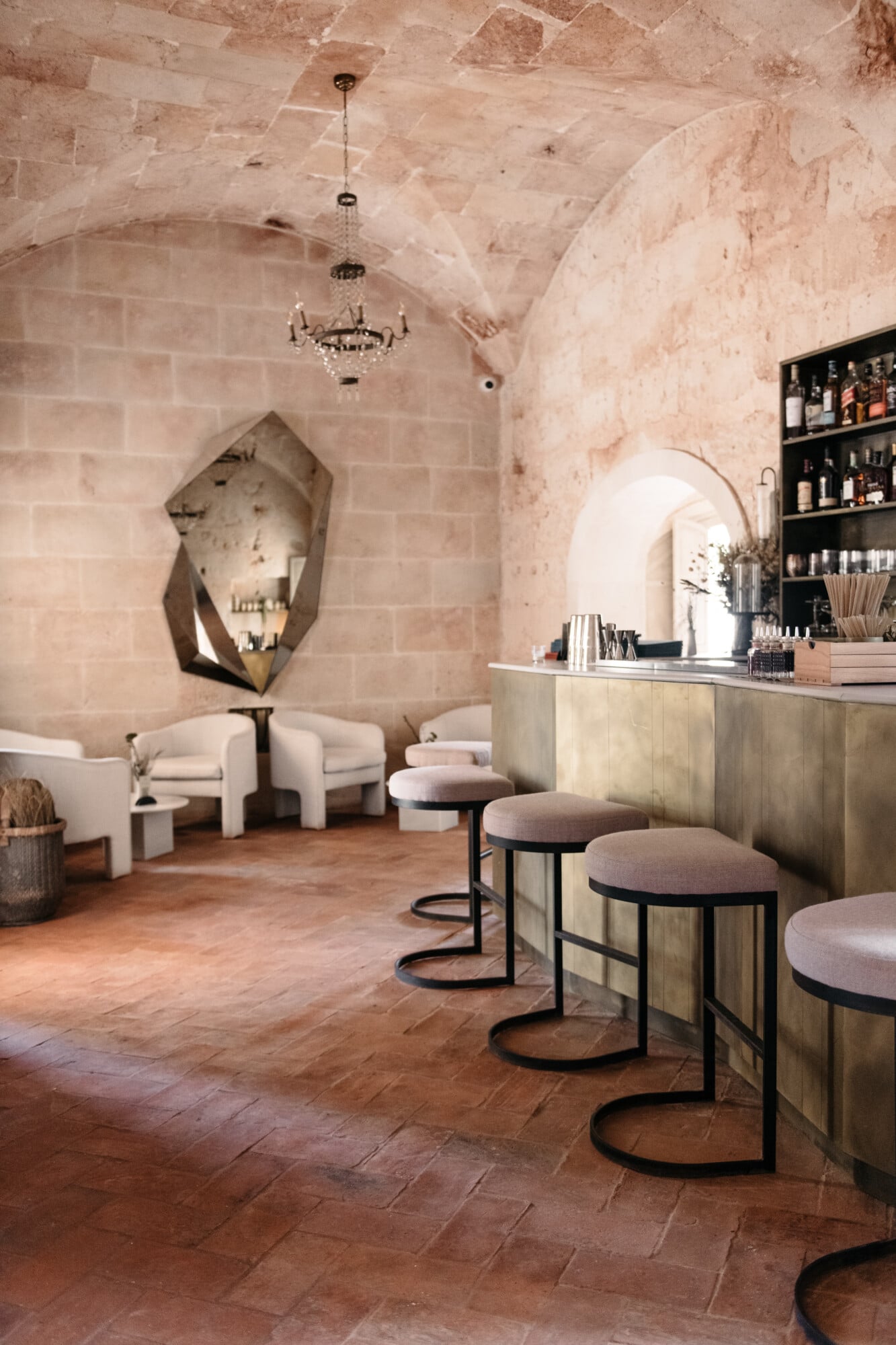 Son Vell, Balearic Islands — Vaulted stone spa with curved archways, terracotta floors, cream barrel chairs, brass bar counter, and crystal chandelier.