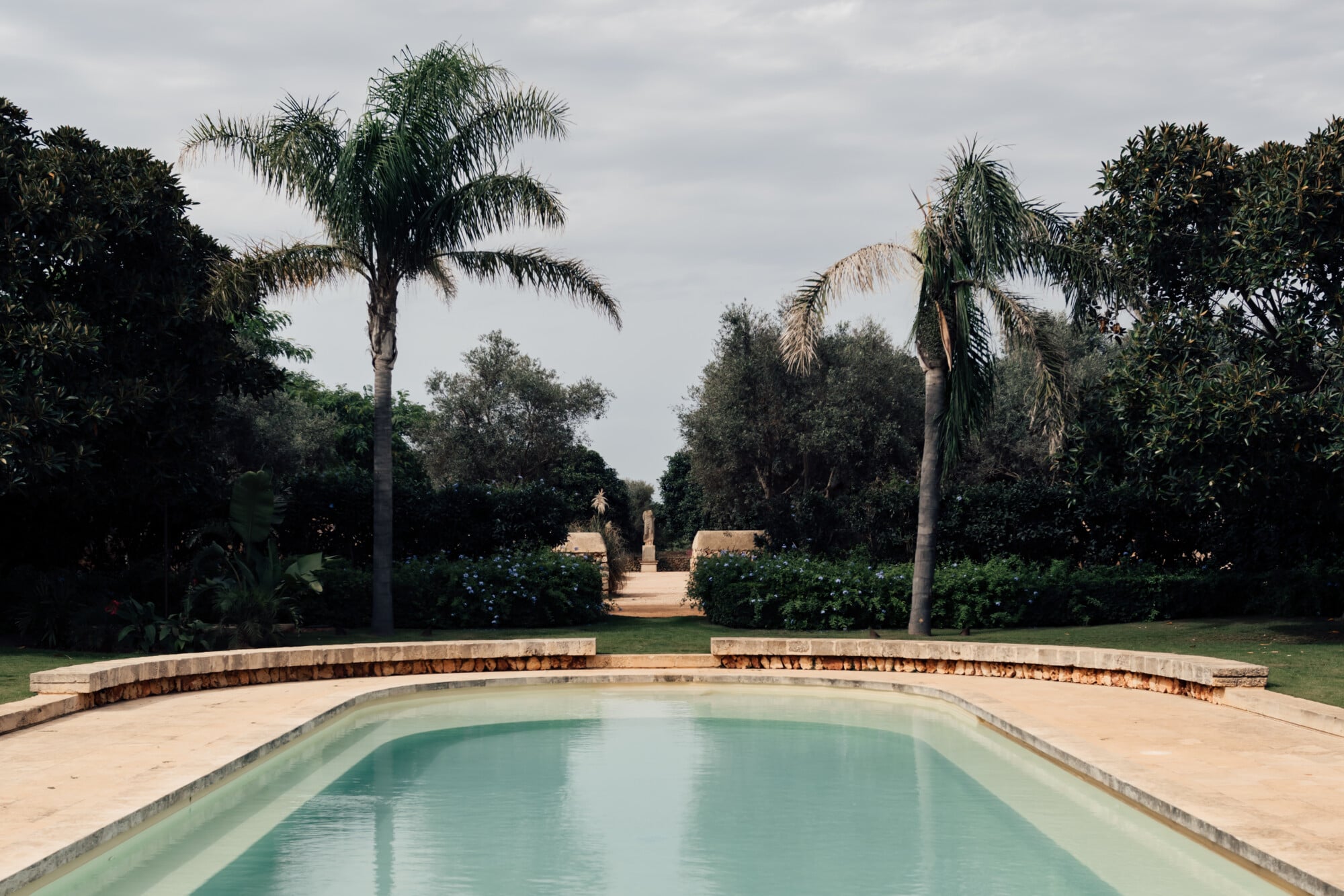 Son Vell, Balearic Islands — Rectangular pool with turquoise water, curved stone edge, palm trees, manicured gardens, Mediterranean estate architecture and landscape design.
