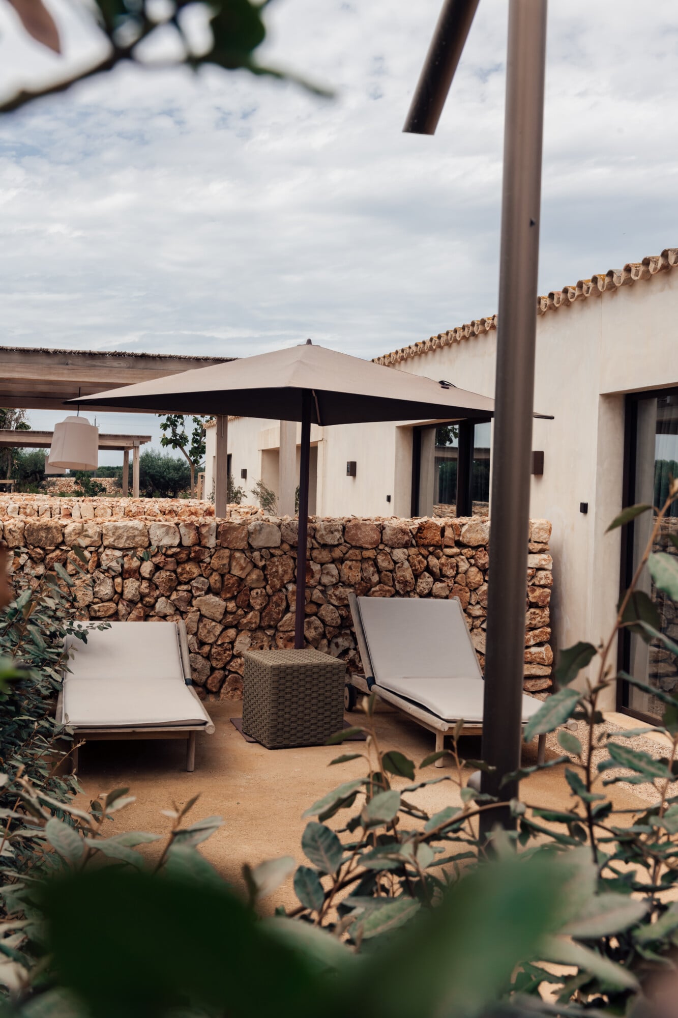 Son Vell, Balearic Islands, Spain — Minimalist terracotta courtyard with loungers, black cantilever umbrella, stone walls, and contemporary architecture under Mediterranean light.
