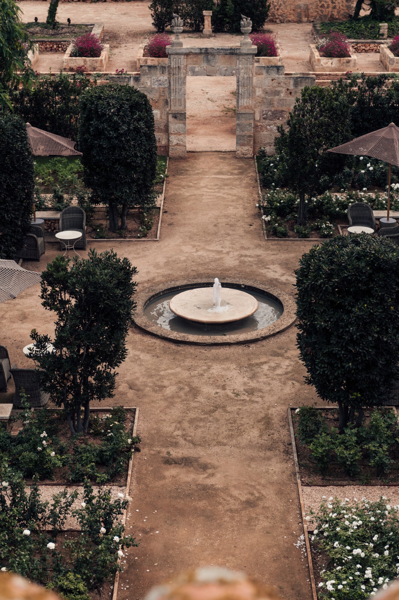 Son Vell, Balearic Islands, Spain — Symmetrical courtyard with central fountain, manicured hedges, terracotta pathways, and stone archway framing Mediterranean garden design.