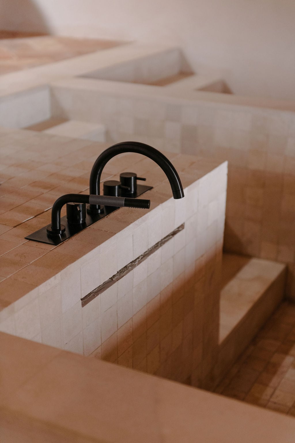 Son Vell, Balearic Islands — Black arc faucet installed in recessed limestone sink basin with white tile surround, minimalist luxury bathroom detail.