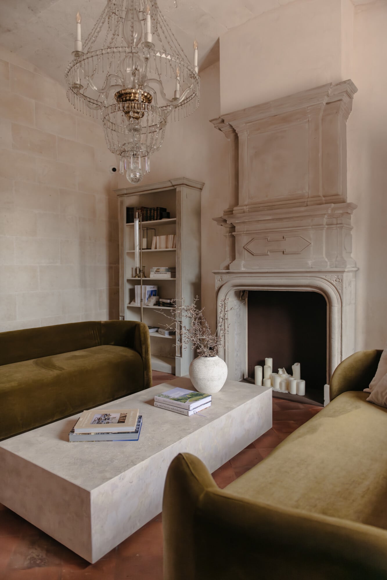 Son Vell, Balearic Islands — Cream living room with brass chandelier, stone fireplace, olive velvet seating, and classical architectural details.
