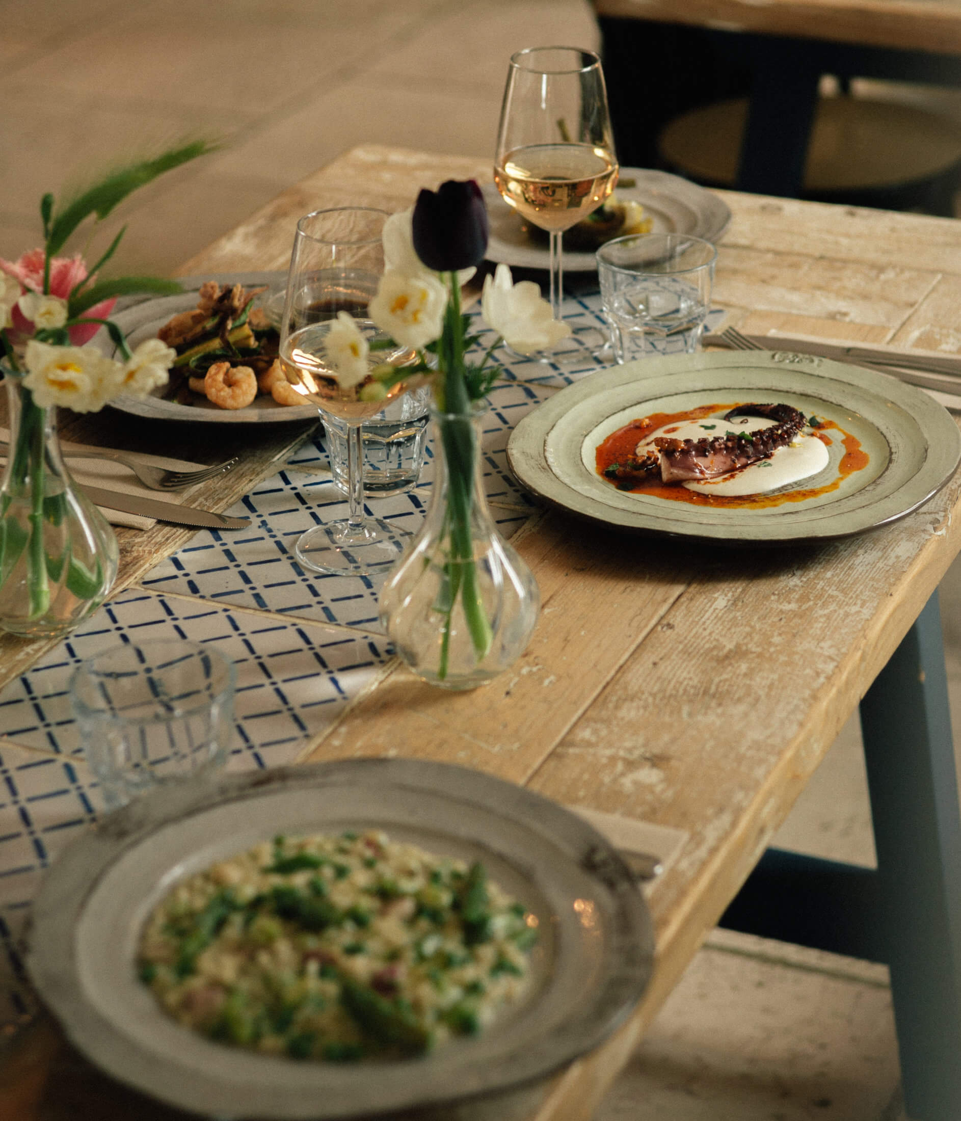 Osteria San Michele, Europe — Fine dining table with plated fish, salad, white wine, fresh flowers, and blue-patterned runner on natural wood surface.