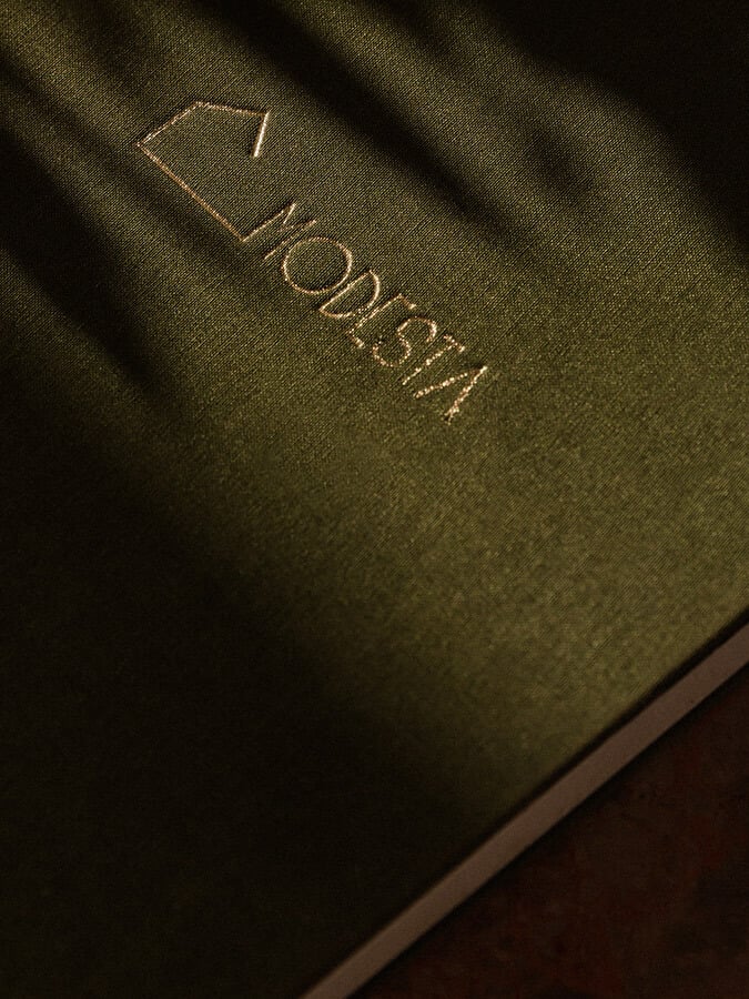 Casa Modesta, Europe — Gold-embossed leather journal cover in olive-green under warm sunlight, luxury hospitality branding detail.
