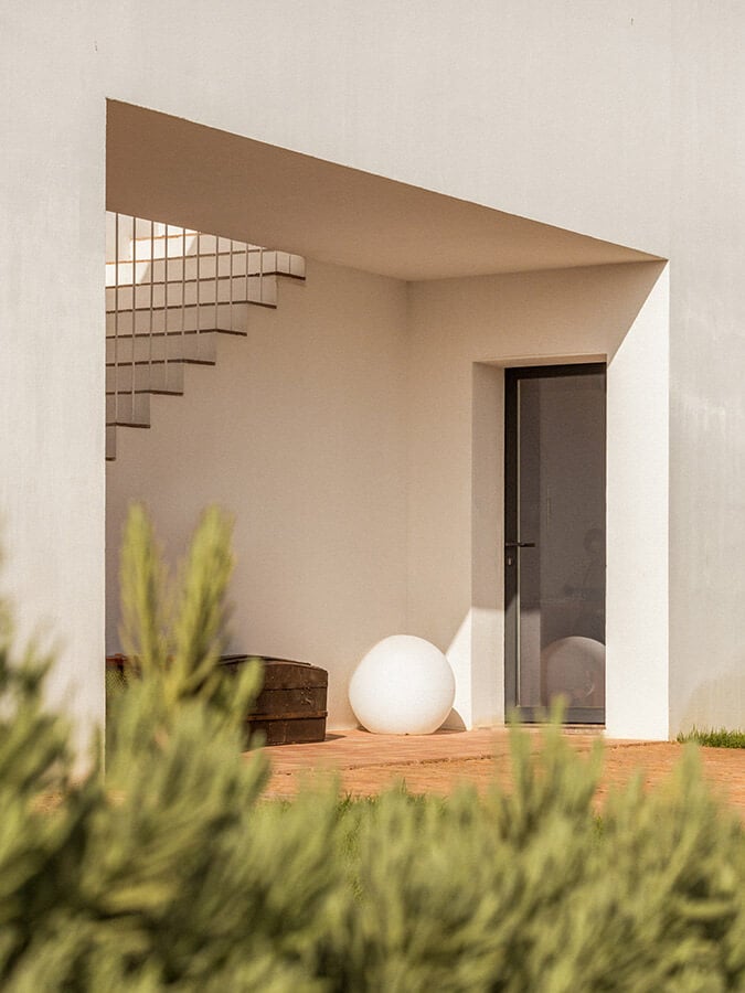 Casa Modesta, Europe — Minimalist white cubic architecture with wooden terrace, sculptural sphere lighting, and geometric lattice detail in Mediterranean sunlight.