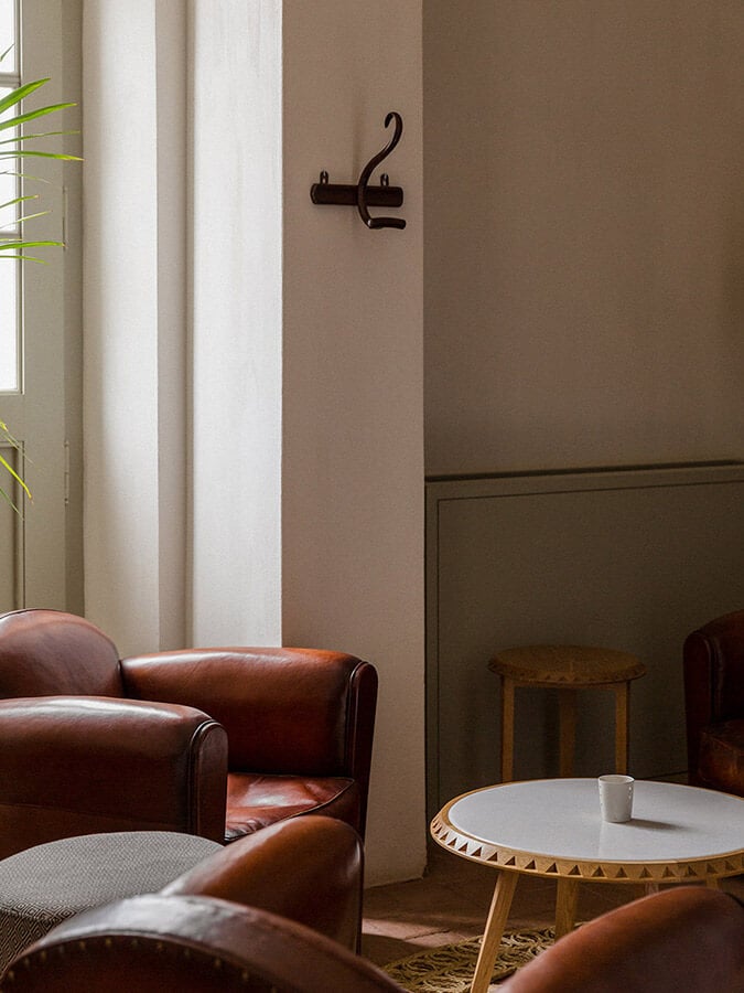 São Lourenço do Barrocal, Portugal — Minimalist lounge with cognac leather armchairs, round travertine table, and sculptural wall hooks against taupe and cream walls.