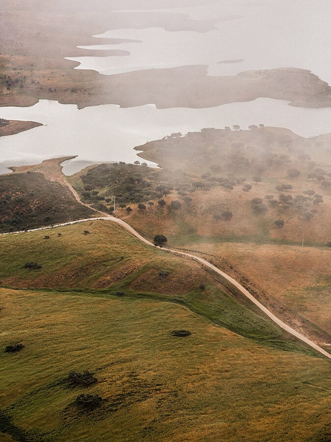 São Lourenço do Barrocal, Portugal — Aerial view of rolling green hills, geometric water reservoirs, and misty landscape with architectural interventions cutting through terrain.