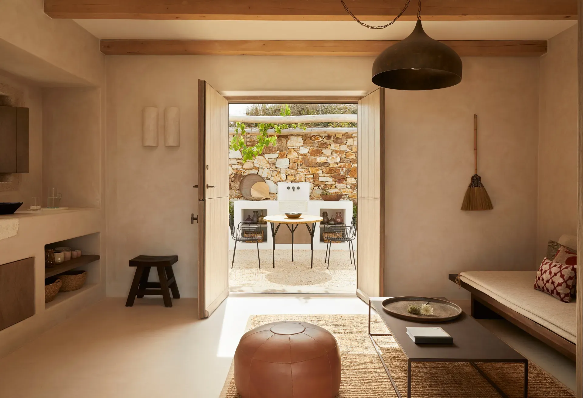 The Rooster, Europe — Minimalist villa bedroom with stone courtyard view, warm plaster walls, wooden beams, natural light, woven textures, mid-century furnishings.