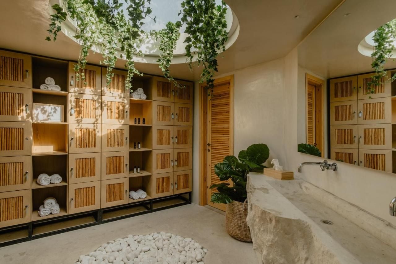 Asana Yoga Shala, Europe — Spa bathroom with timber storage cubbies, marble soaking tub, cascading hanging plants, and minimalist Japanese-inspired design.