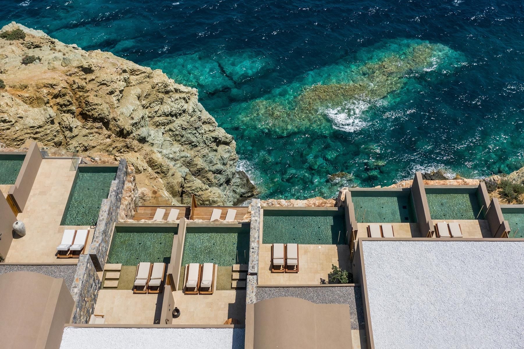 ACRO Suites, Europe — Terraced stone suites with striped loungers overlooking turquoise Mediterranean waters and limestone cliffs, minimalist coastal architecture.