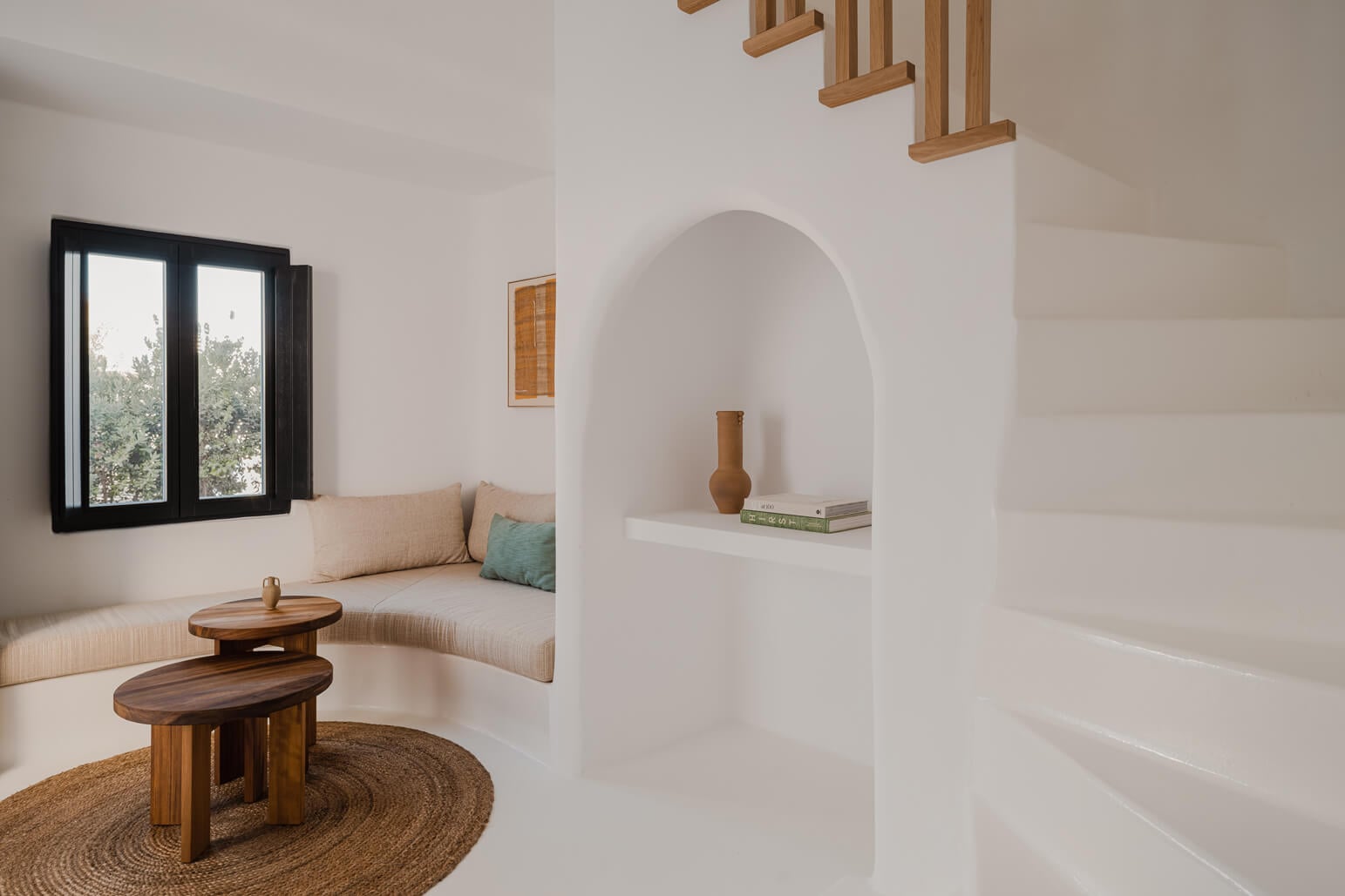 Nobu Santorini, Europe — Minimalist whitewashed alcove with curved archway, wooden side table, natural linen seating, terracotta vessels, and black-framed window overlooking landscape.