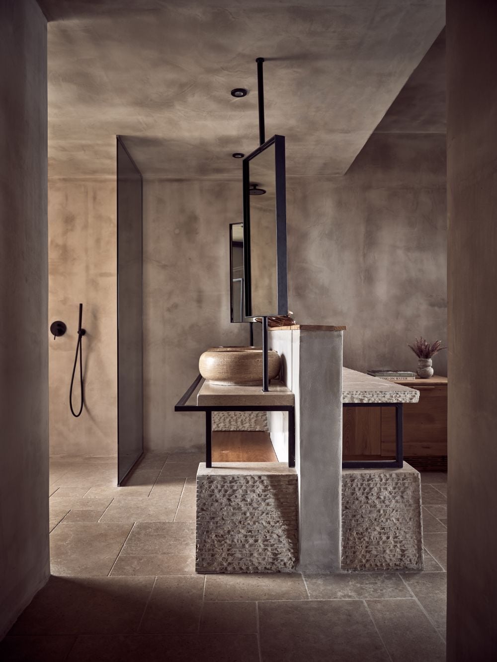 ACRO Suites, Europe — Minimalist bathroom with concrete walls, vessel sink on wooden shelf, black metal frame mirror, terrazzo basin details, and walk-in shower.