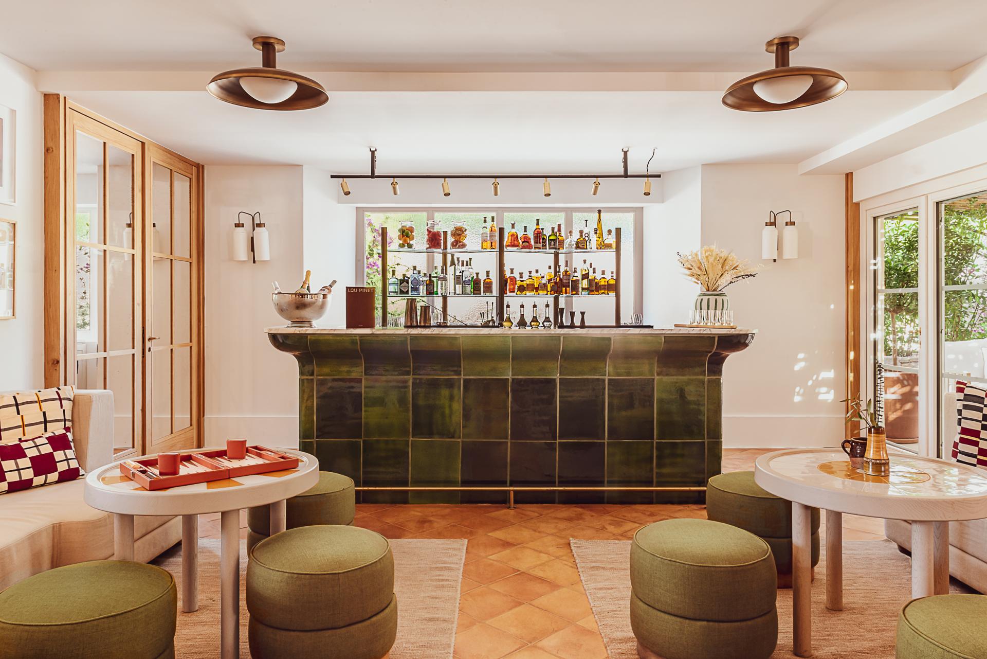 Hôtel Lou Pinet, Europe — Brass bar counter with stocked shelves, olive-green seating, natural wood furnishings, and terracotta flooring in luxury hospitality lounge.