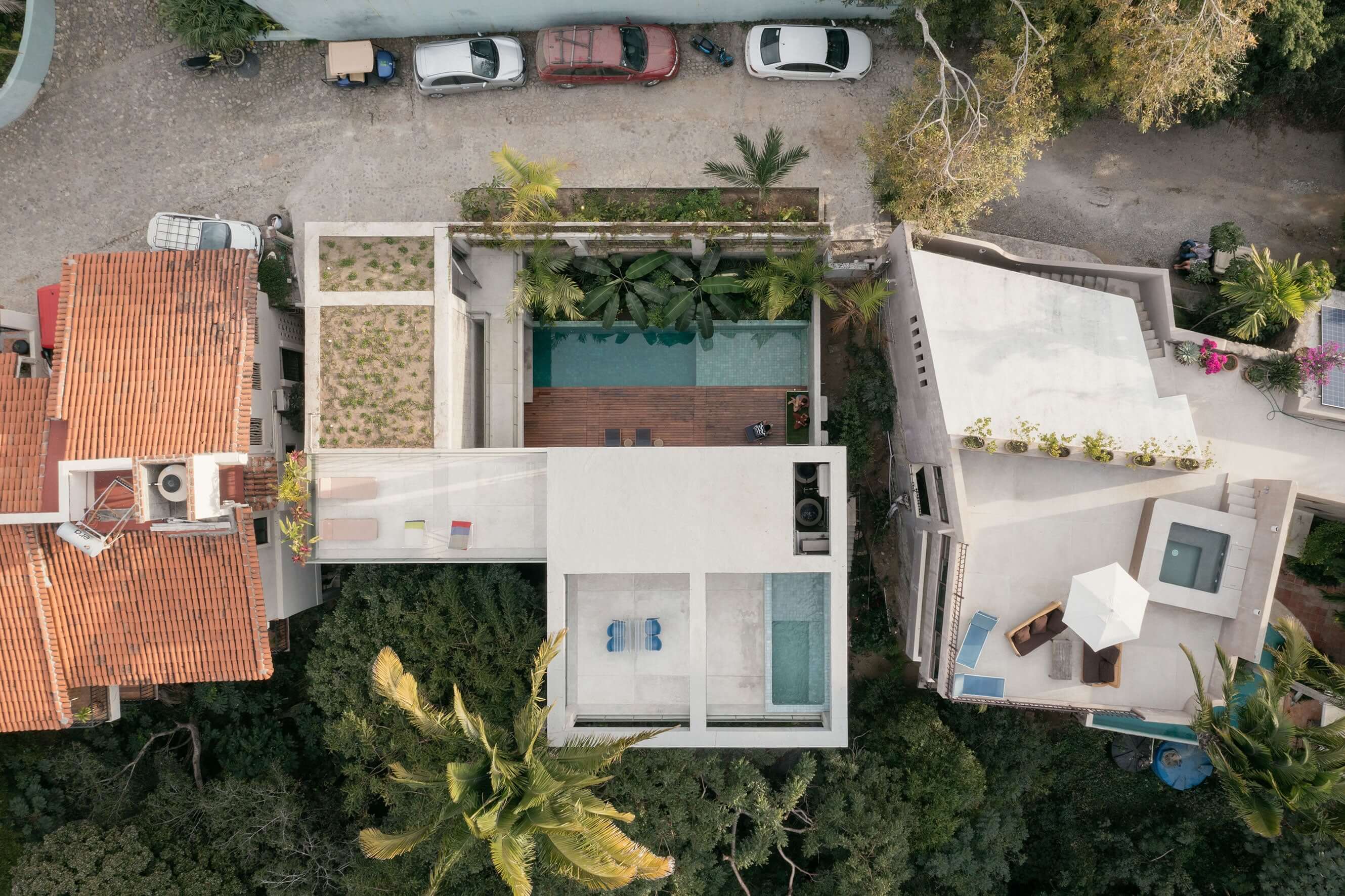 NICO, Mexico — Aerial view of modernist residence with turquoise pool, palm trees, white concrete terraces, and red-tile neighboring architecture in urban courtyard setting.