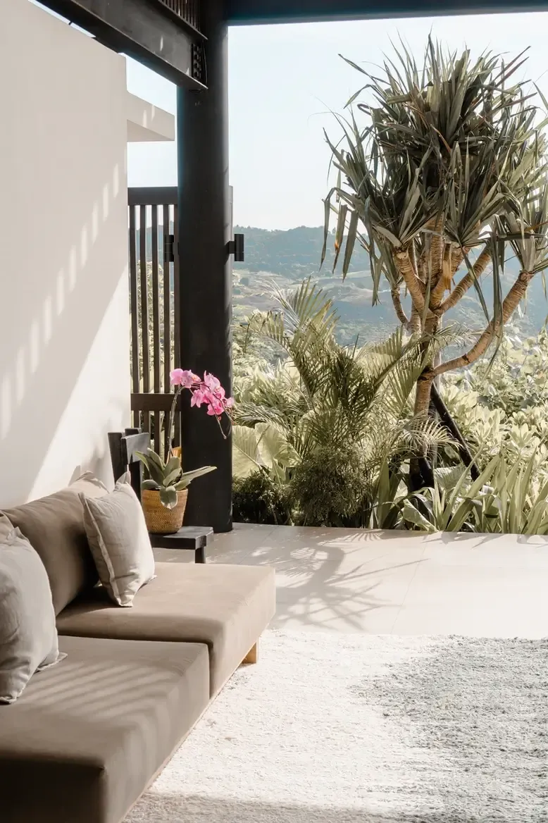 Somewhere Lombok, Asia — Minimalist terrace with cream linen seating, tropical plants, and mountain valley views framed by black timber architecture and natural light.
