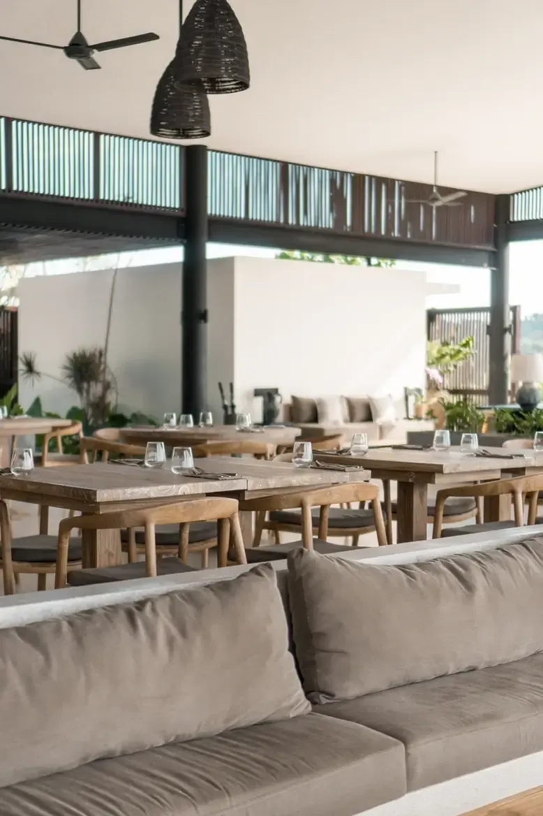 Somewhere Lombok, Asia — Open-air dining pavilion with teak tables, woven pendant lights, and tiered deck overlooking tropical landscape.