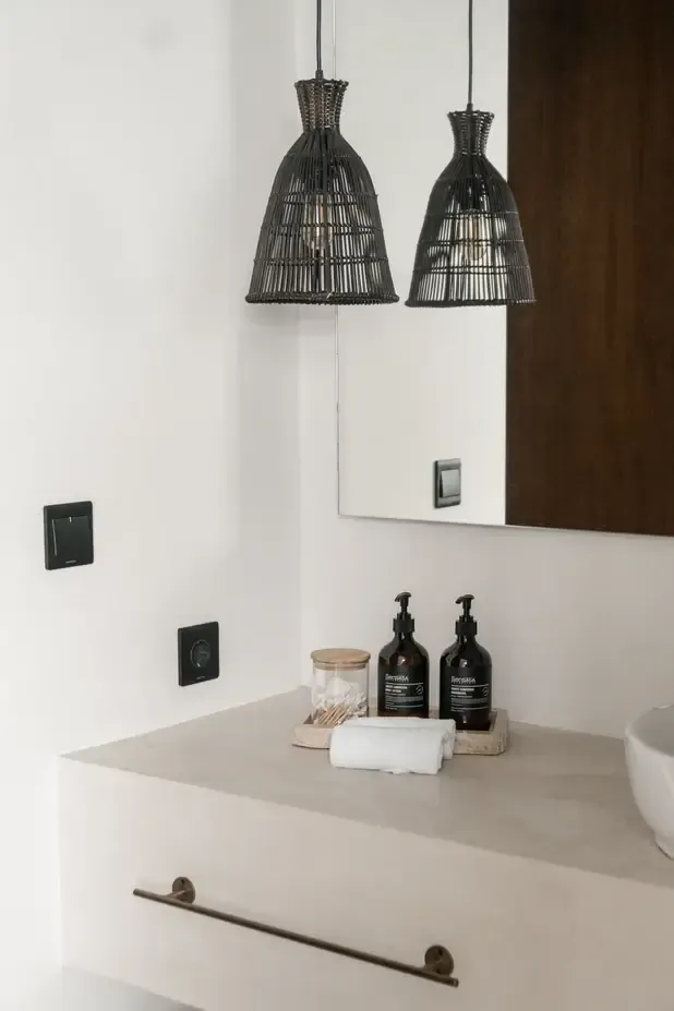 Somewhere Lombok, Asia — Modern bathroom vanity with woven black pendant lights, marble countertop, black amenity bottles, and minimalist fixtures.