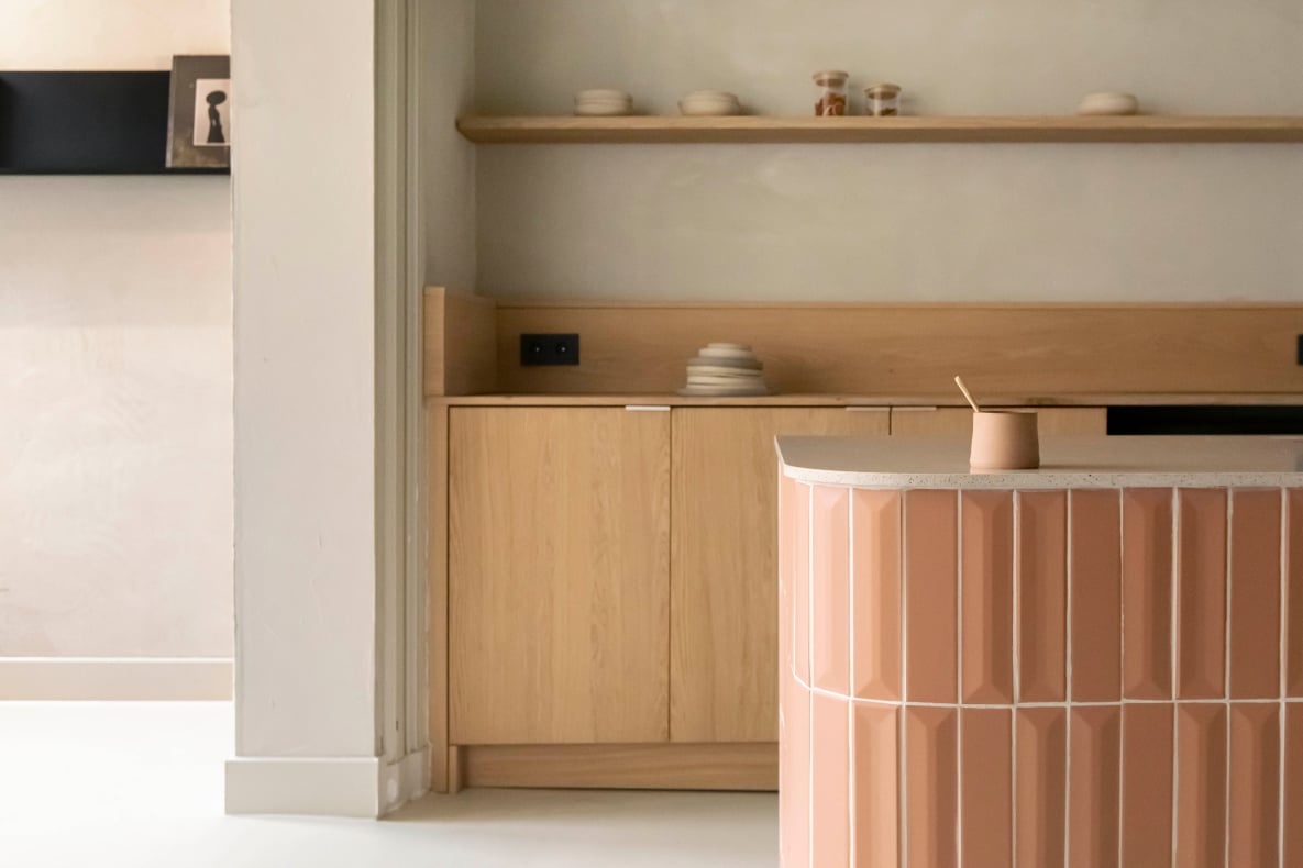Hotel âme, Europe — Minimalist reception desk in natural wood with cream stone countertop, white metal crib, floating shelves, and soft neutral lighting.