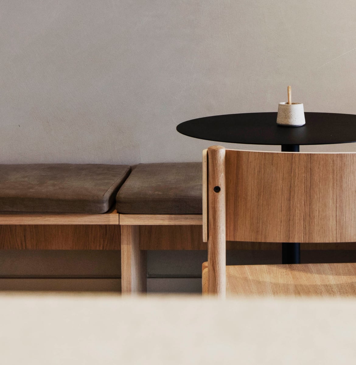Hotel âme, Europe — Minimalist hospitality lounge with walnut bench, black round table, natural light, and ceramic accessory on neutral backdrop.